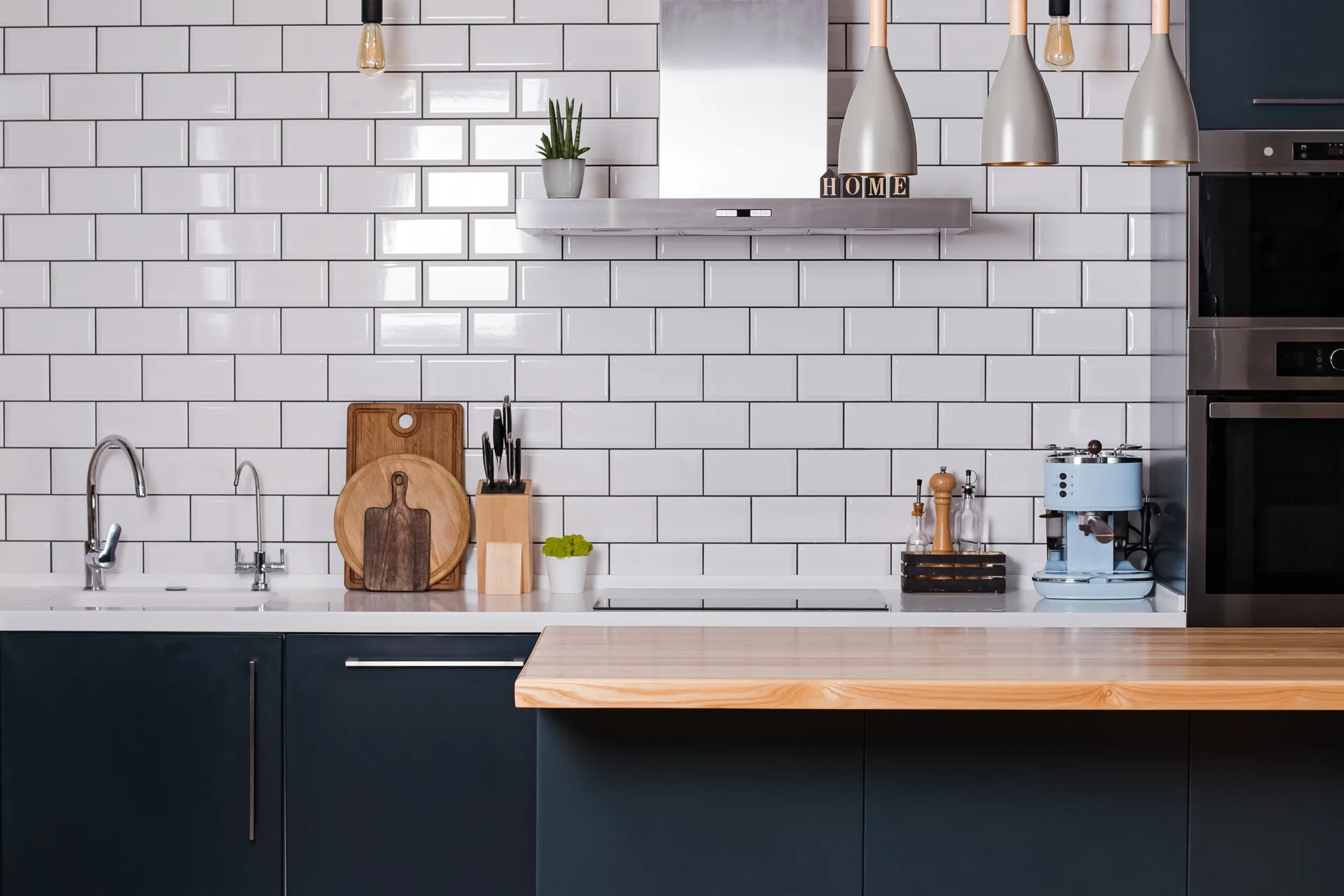 A modern kitchen featuring navy lower cabinets, a white subway tile backsplash with dark grout, and a light wood countertop island.