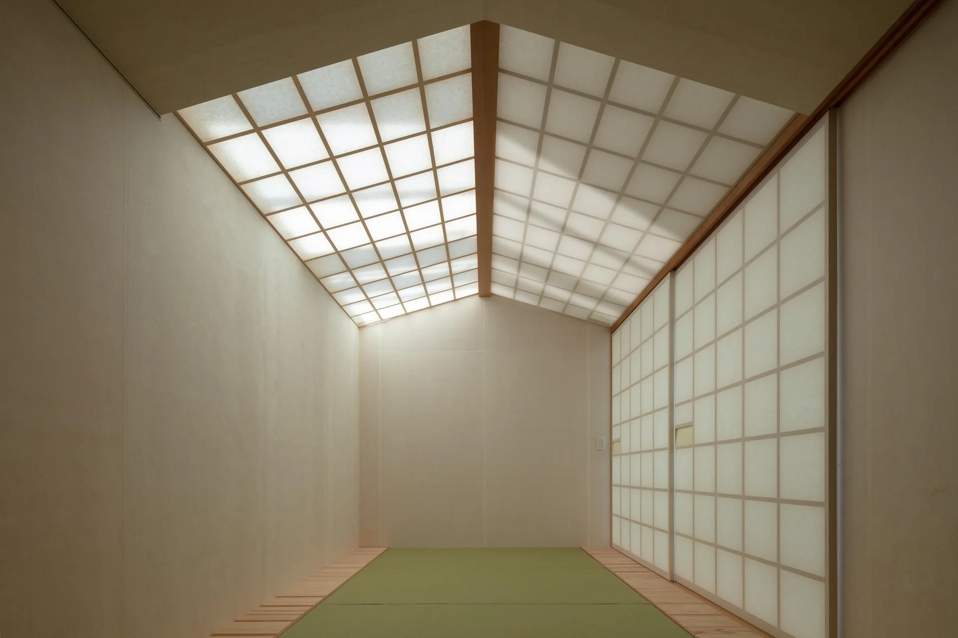 A minimalist Japanese room featuring green tatami mats on the floor, sliding paper shoji doors, and a pitched ceiling made of illuminated grid panels.