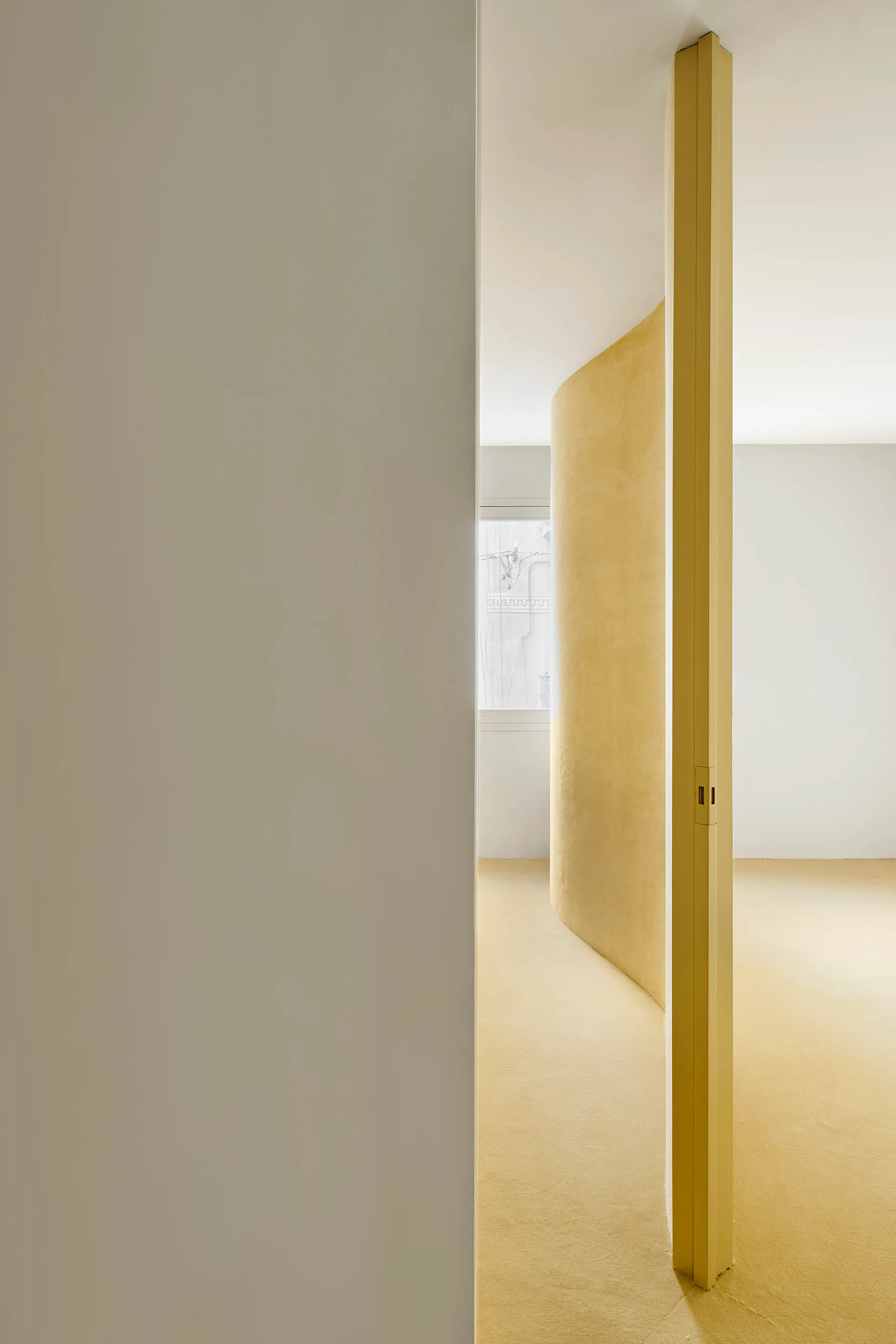 A minimalist interior space features a curved yellow partition wall rising from a matching yellow floor, framed by smooth white walls.