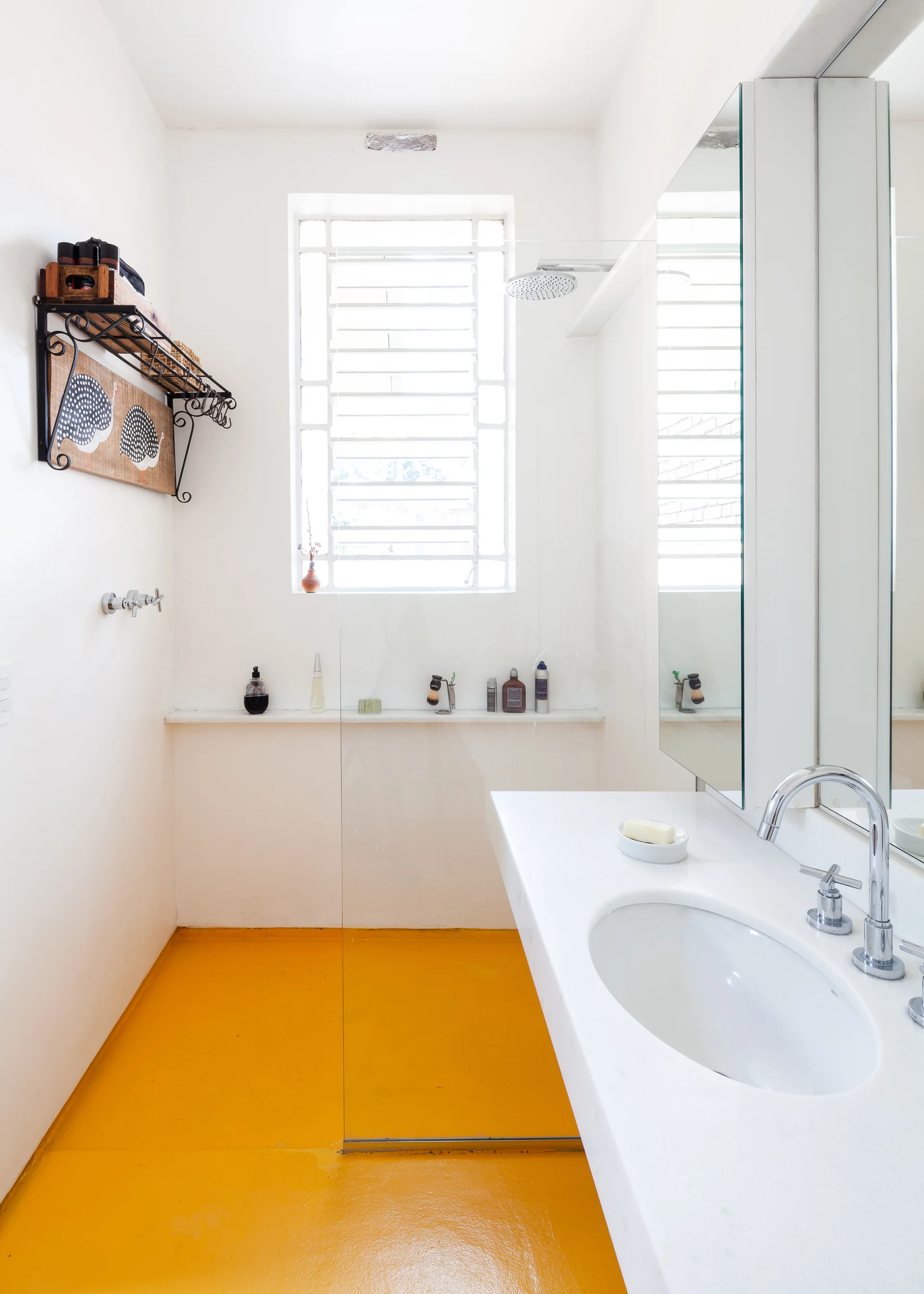 A minimalist white bathroom with a glossy bright yellow floor, a chrome faucet on a white vanity, and a glass shower partition screen.