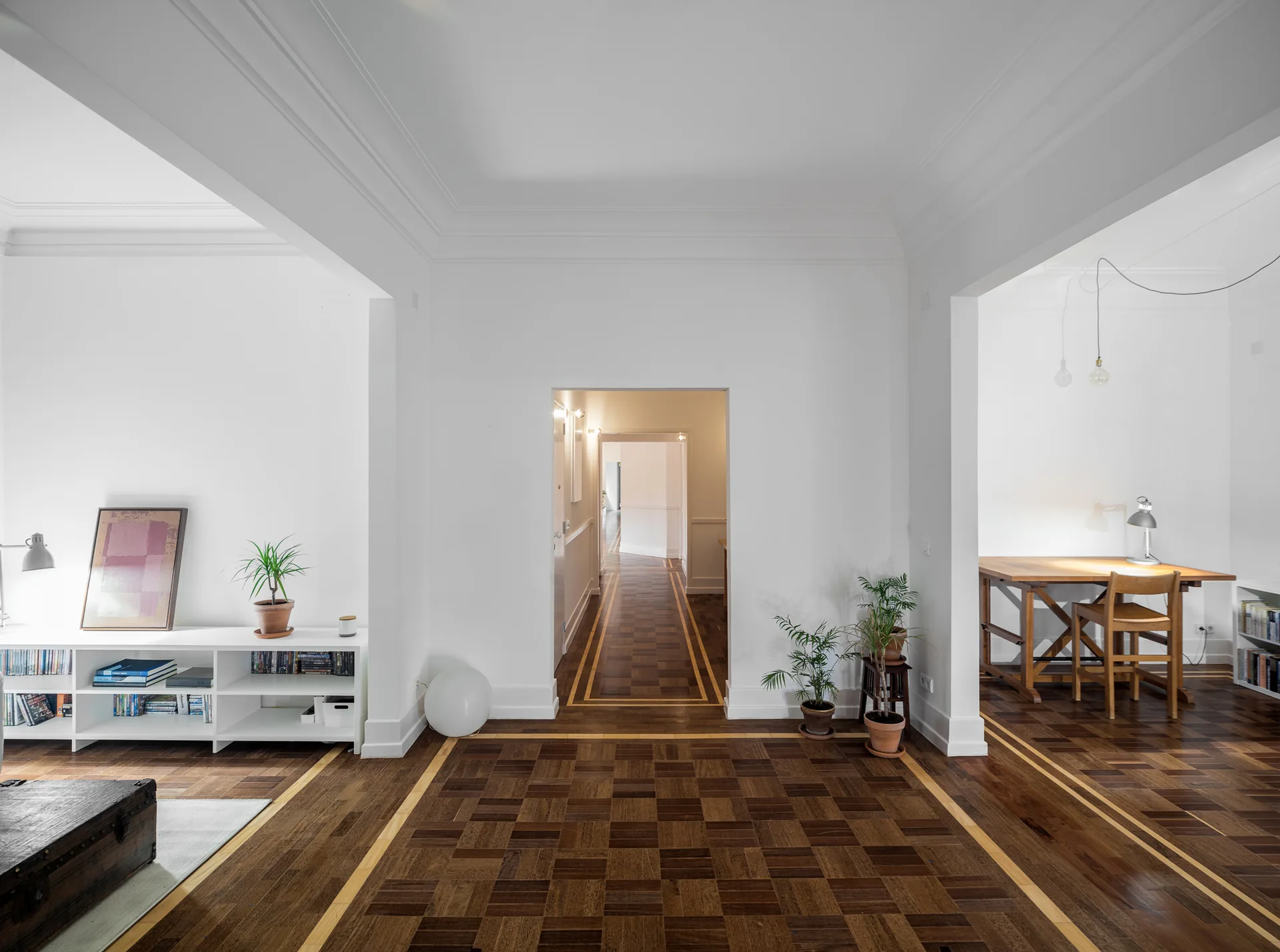A minimalist apartment interior with white walls, dark parquet floors with inlaid light wood borders, and wide arched openings.