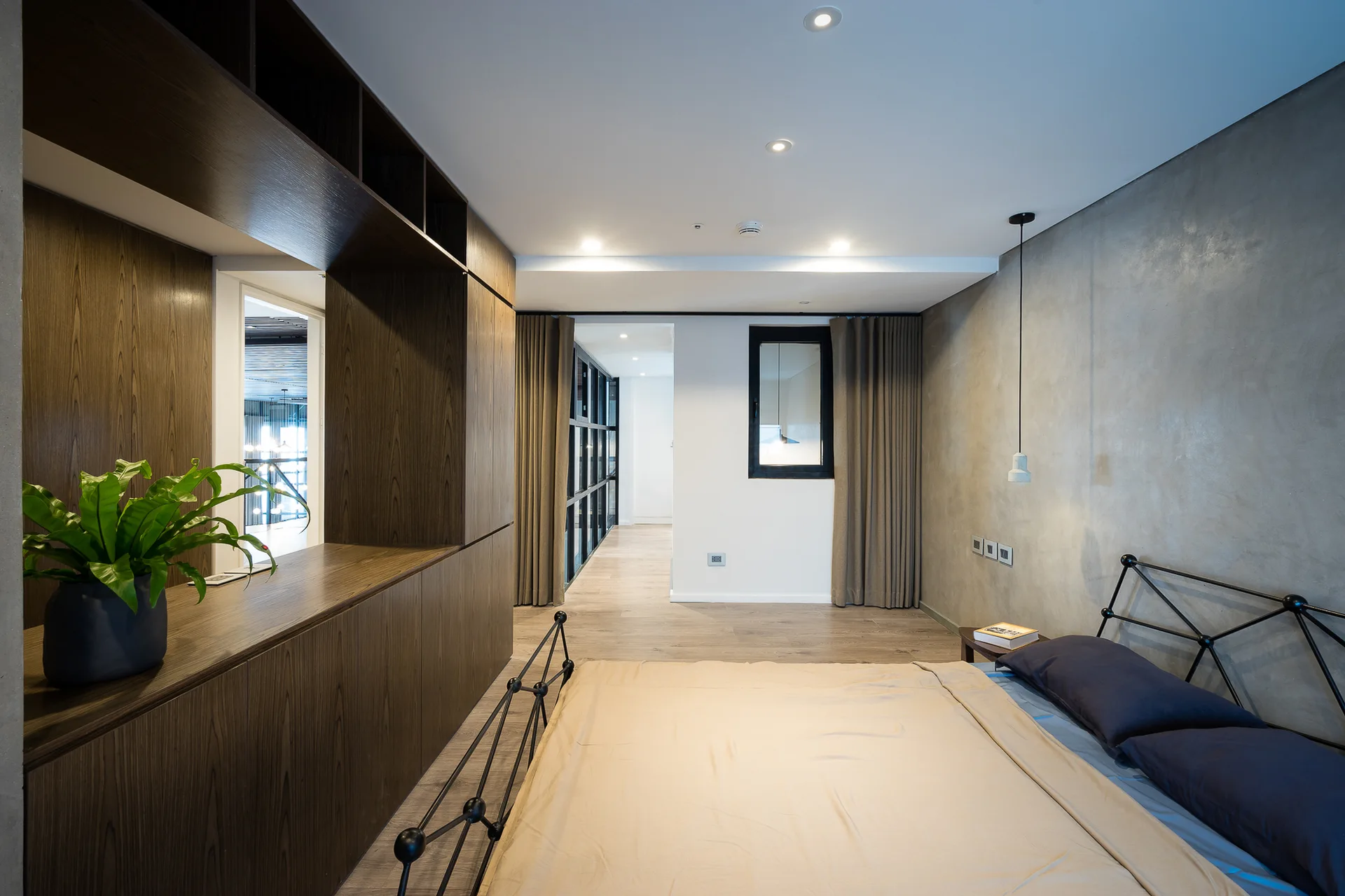 A modern bedroom features a gray concrete wall, a black metal bed frame with beige bedding, and a large dark wood built-in wardrobe unit.