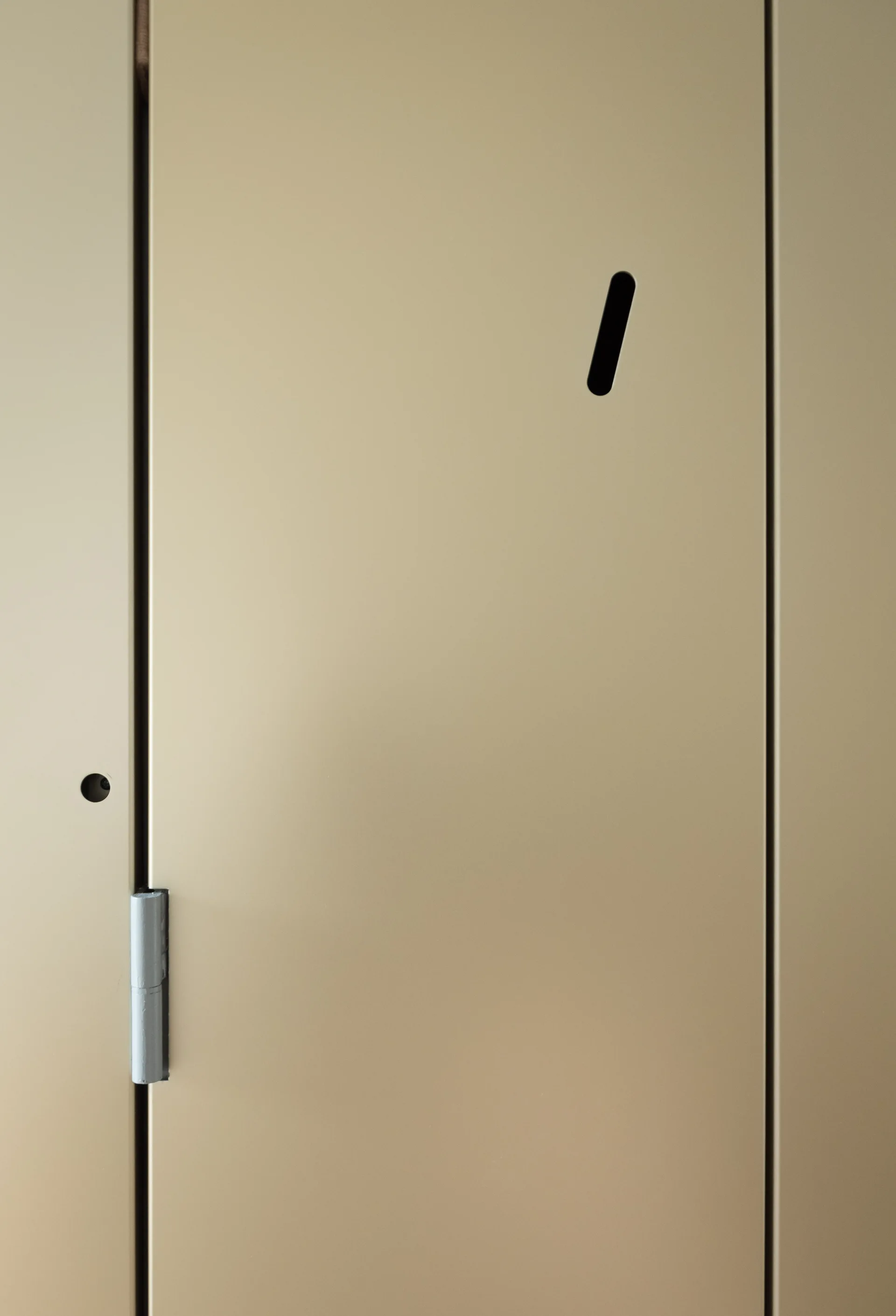 A close-up shot of a matte gold door panel featuring an integrated angled cutout handle and an exposed silver-colored hinge.