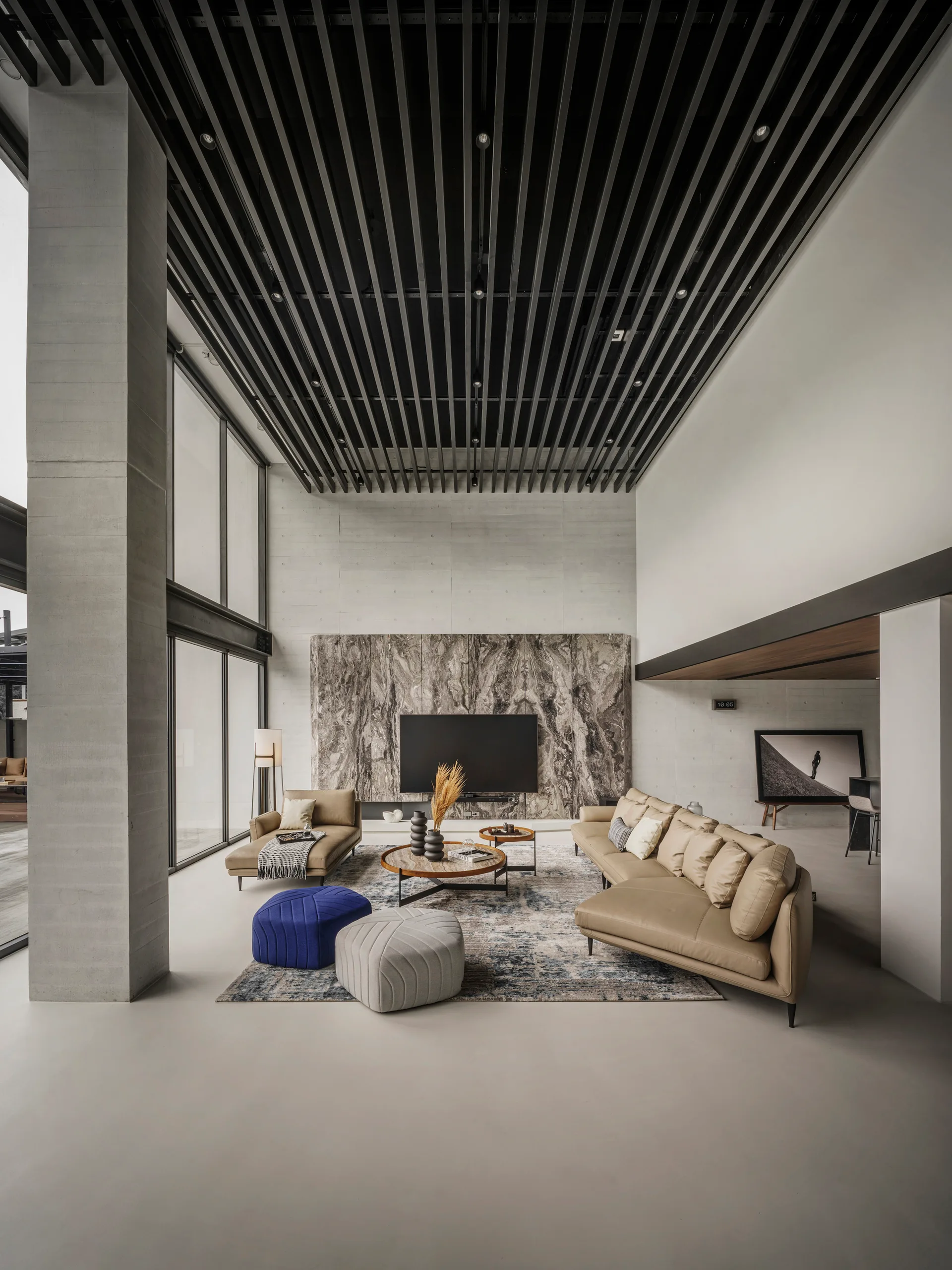 A modern double-height living room with a dark slatted wood ceiling, a large marble TV wall, tan leather sofas, and floor-to-ceiling windows.