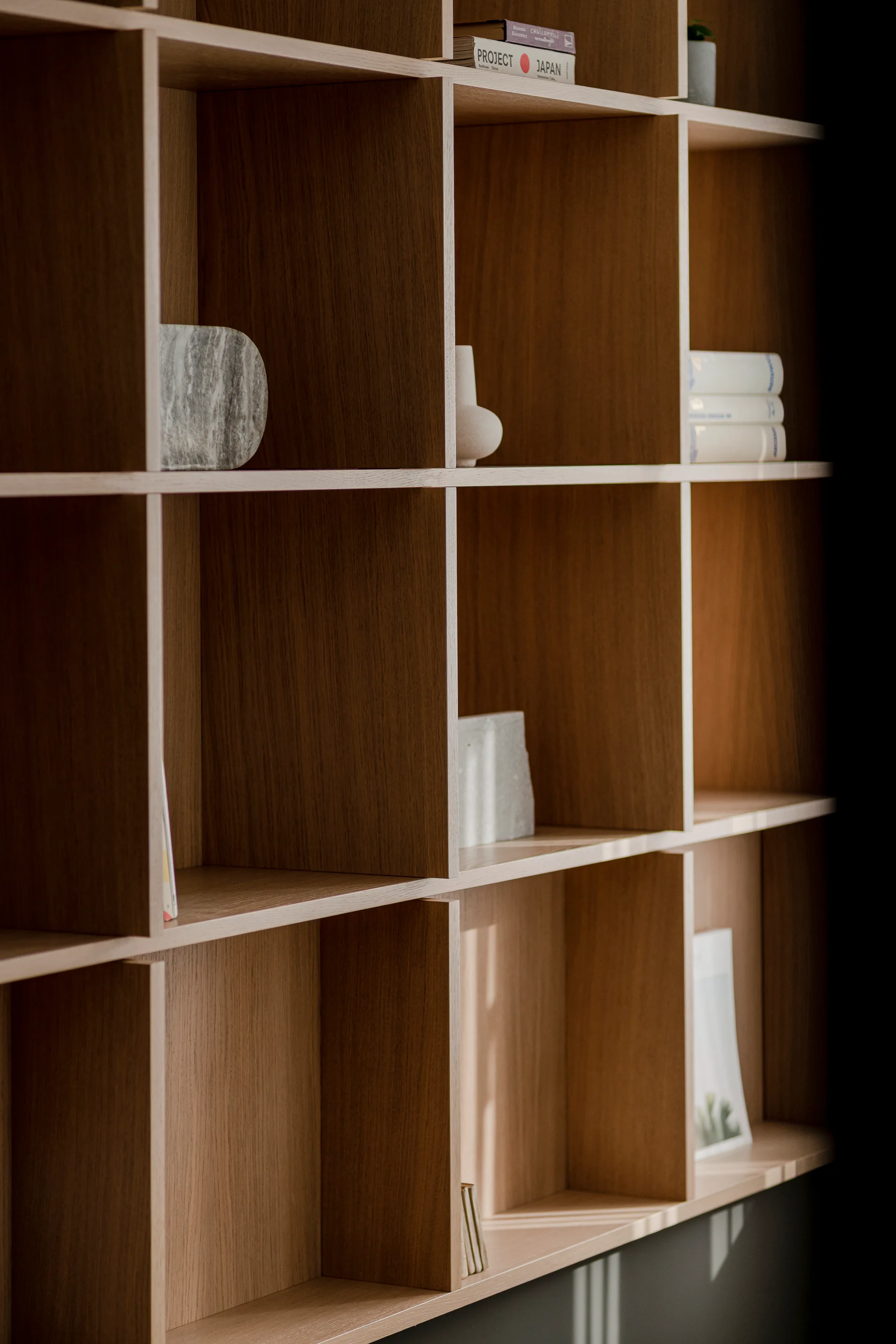 A close-up of a medium-brown wood grid shelving unit styled with a few books, a small ceramic vase, and a grey stone sculpture.