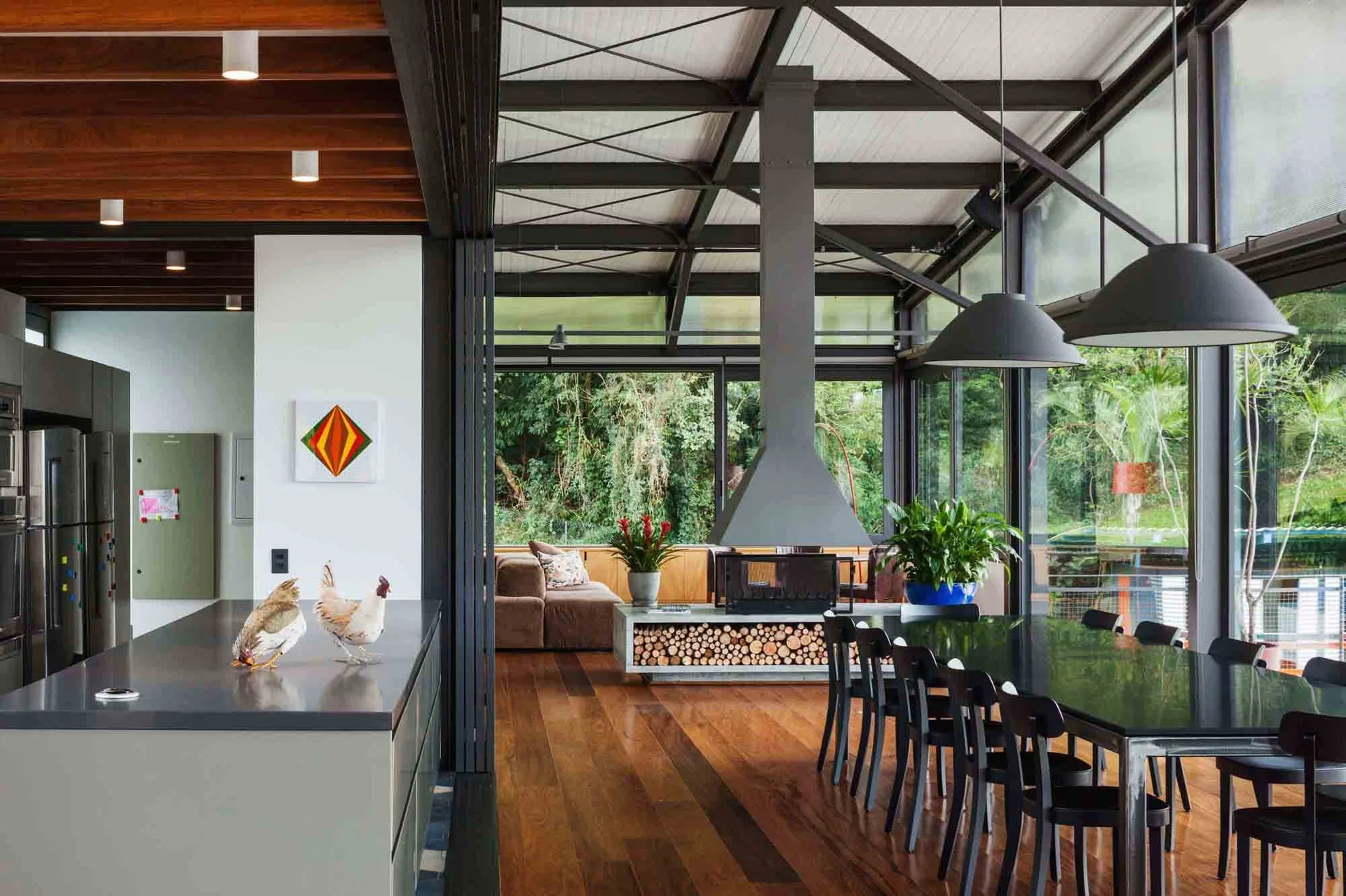 An open-plan dining room features a black dining table, dome pendant lights, and a central modern fireplace set against floor-to-ceiling windows.