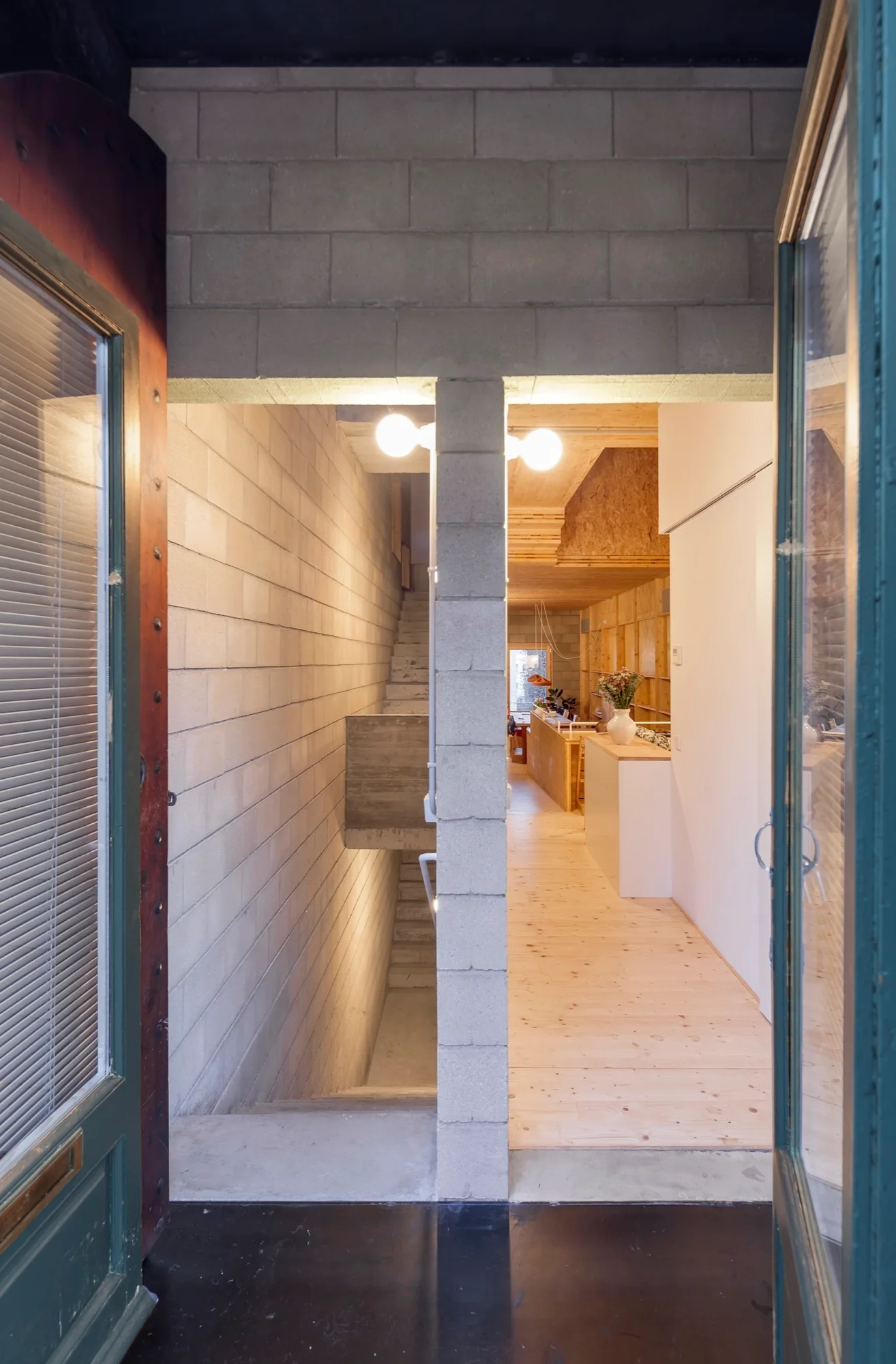 A view through an open door shows a split-level entry with a concrete block stairwell on the left and a warm wood-floored interior on the right.