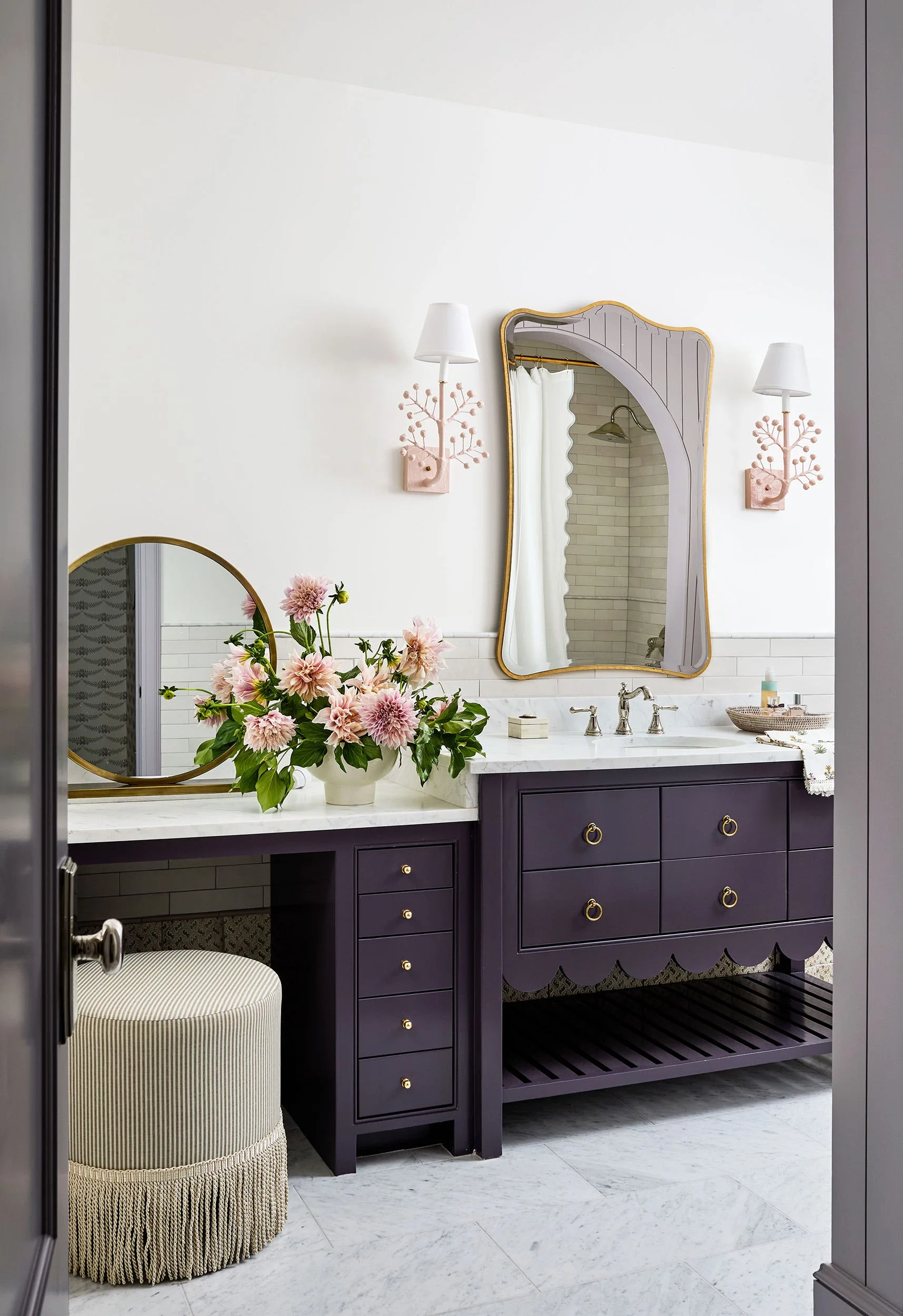 A bathroom vanity area features a deep purple cabinet with a marble top, a scalloped gold mirror, and a fringed striped stool.