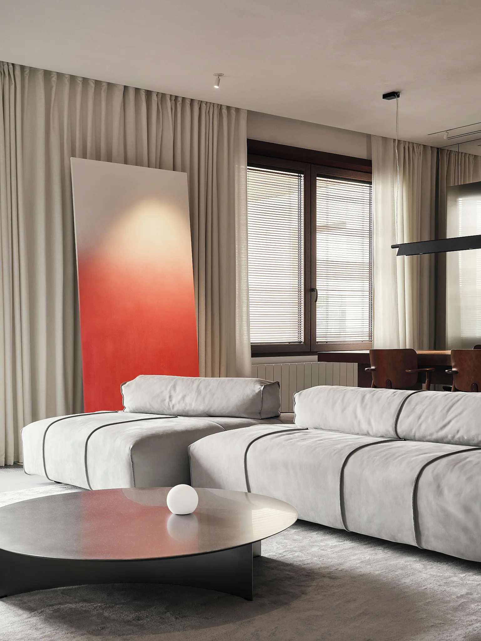 A gray modular sofa faces a low metallic coffee table in a room with beige curtains and a large orange gradient art piece leaning against the wall.