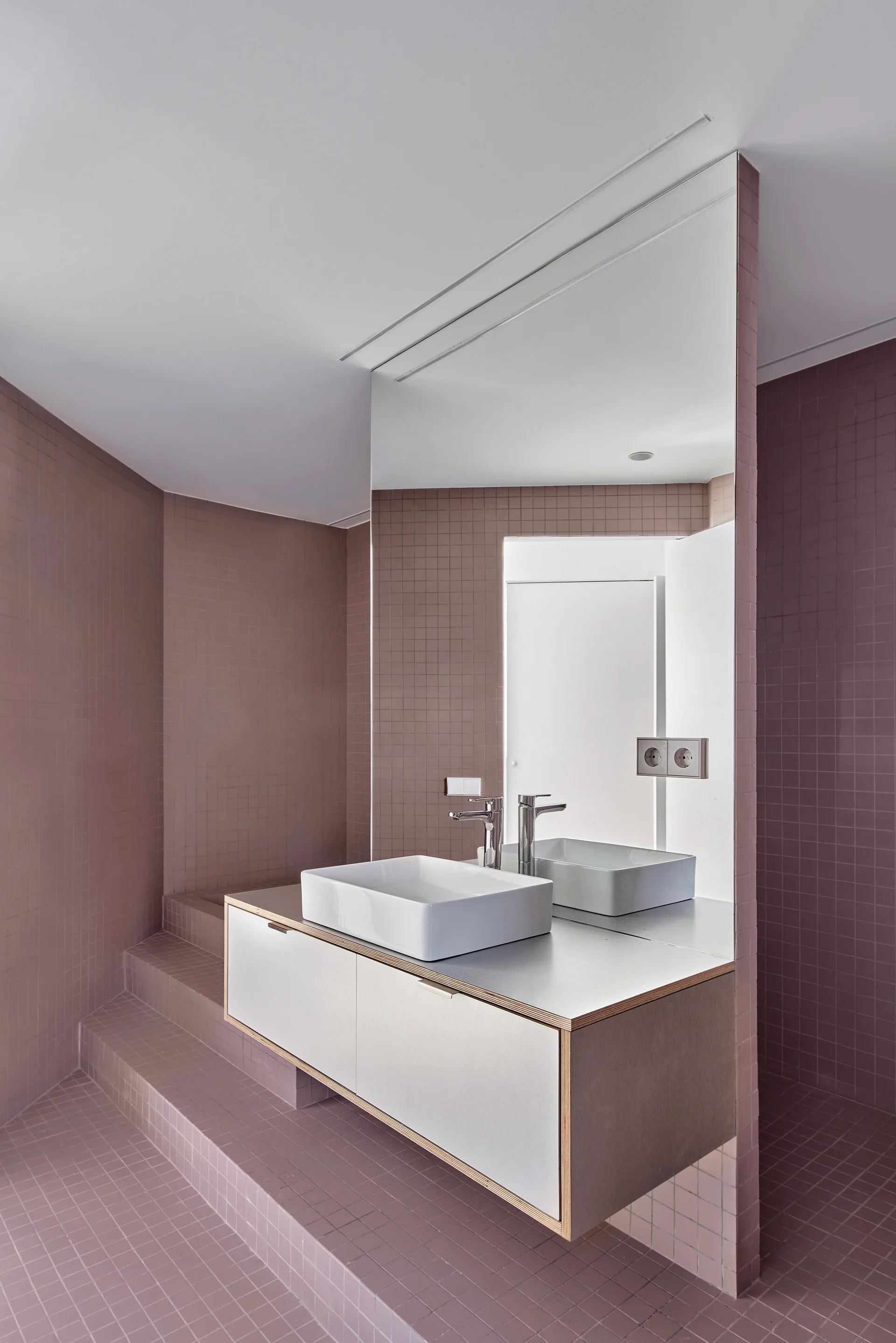 A modern bathroom covered in mauve grid tile featuring a floating white vanity, a rectangular vessel sink, and a large frameless mirror.