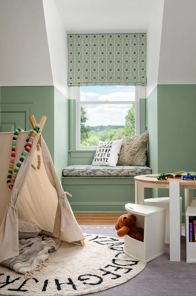 A children's playroom features a green and white two-tone wall, a built-in window seat with patterned cushions, and a small canvas teepee.