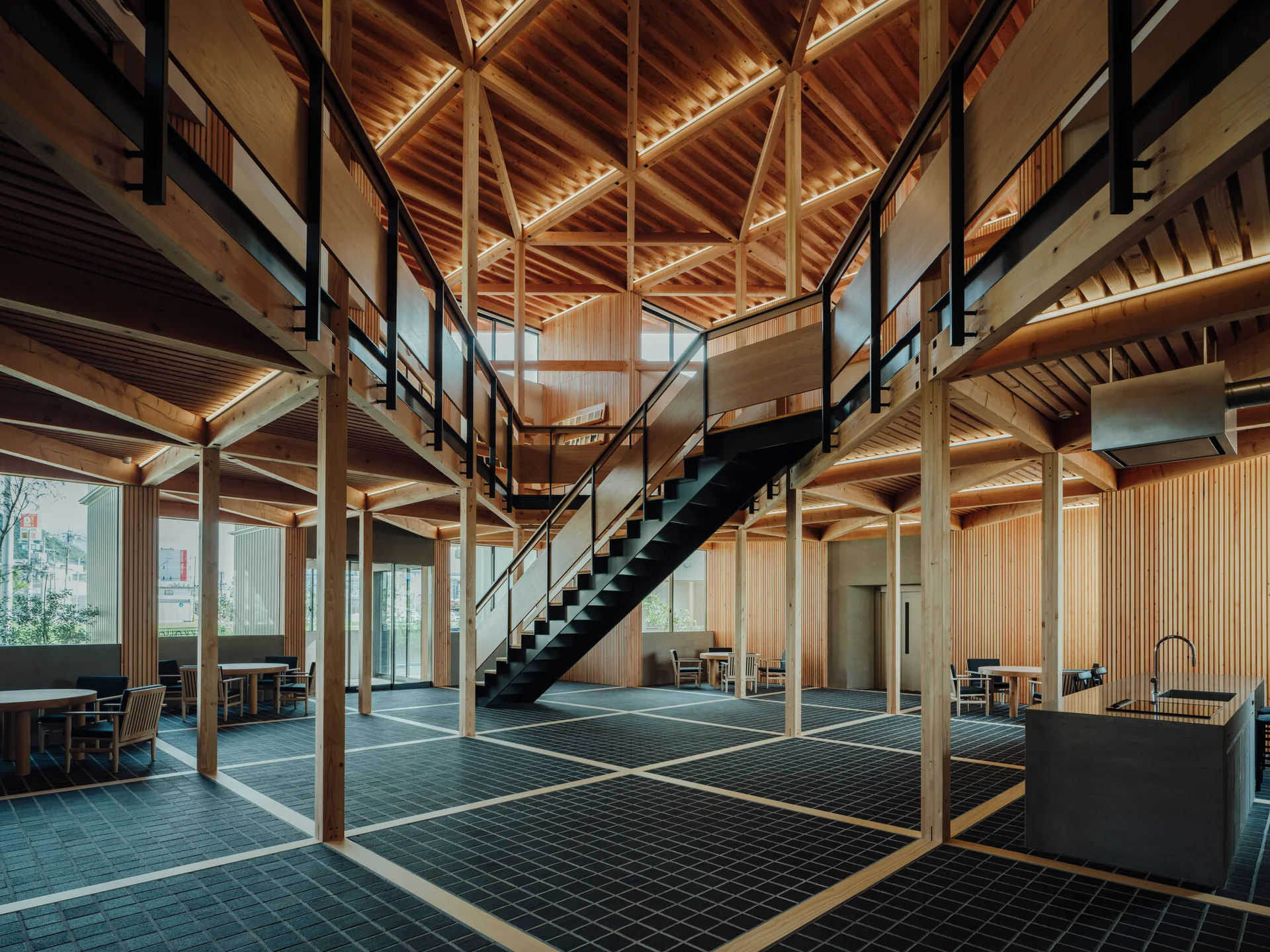 A spacious double-height interior features an intricate exposed timber frame, a central black metal staircase, and dark grid-pattern tiled flooring.