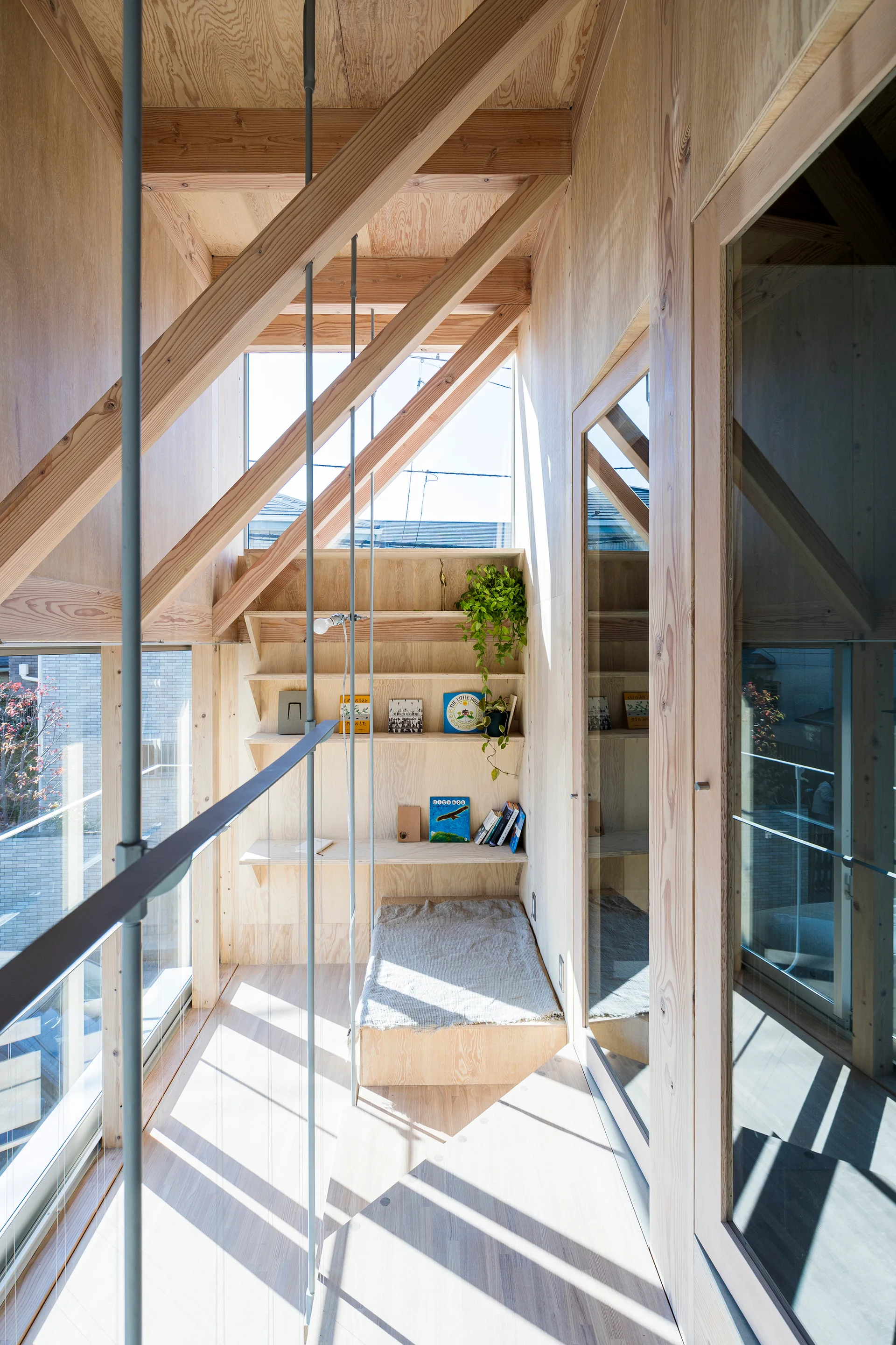 A bright stair landing features light plywood walls, built-in wooden bookshelves, a low daybed platform, and exposed overhead beams.