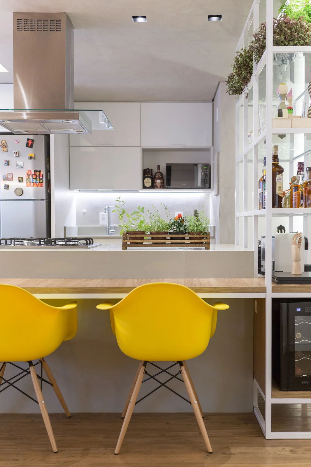 Two bright yellow modern chairs stand at a wood-topped breakfast bar in a kitchen featuring white cabinets and white metal grid shelving.
