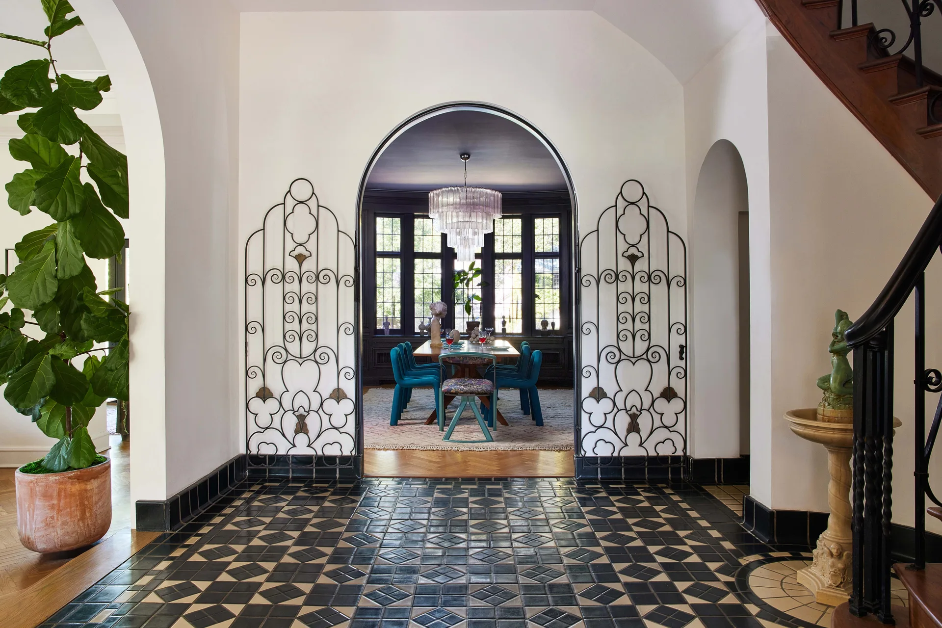 A foyer with black and white geometric floor tiles features a large arched doorway flanked by decorative black wrought iron screens leading to a dining room.
