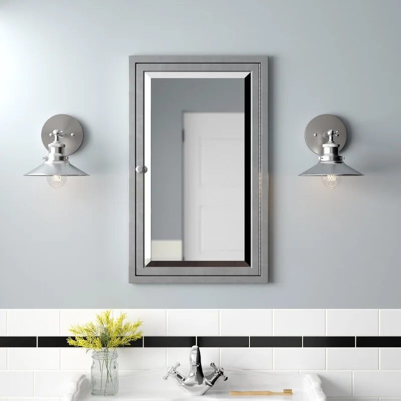 A wall-mounted gray medicine cabinet flanked by two metal wall sconces sits above a white subway tile backsplash with a black accent stripe.