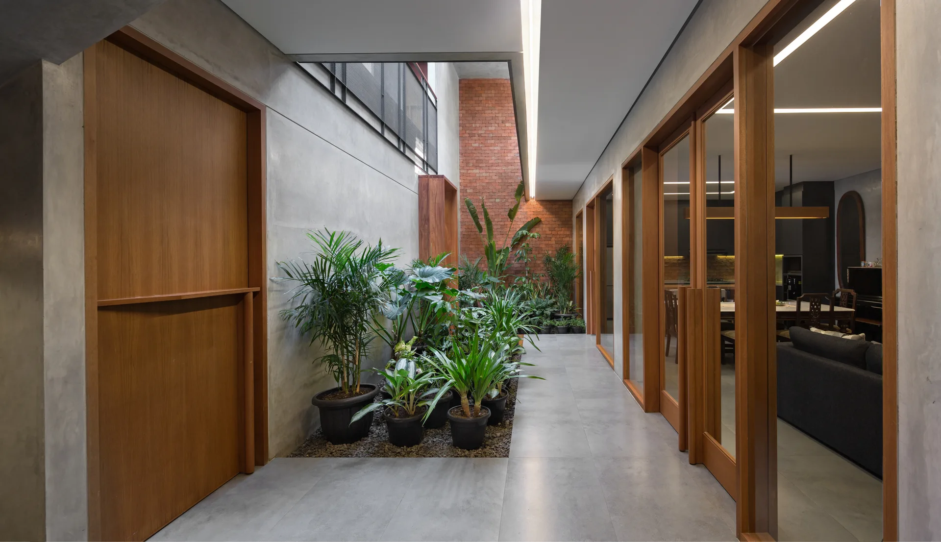 A minimalist indoor hallway features a gravel-lined garden bed with potted plants, concrete walls, and wood-framed glass sliding doors.