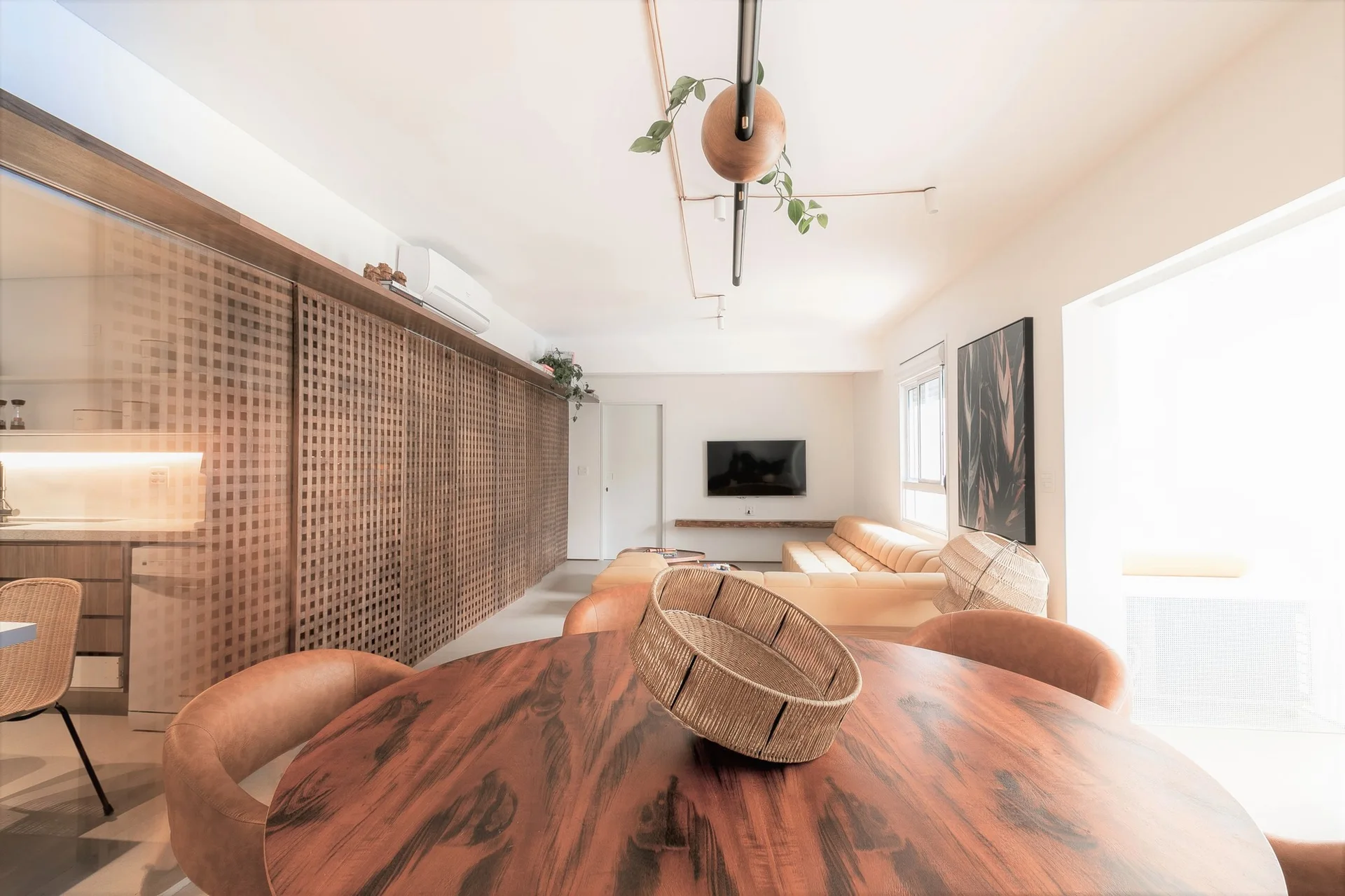 A bright open-plan space featuring a circular wood dining table in the foreground and a large wooden grid partition wall.