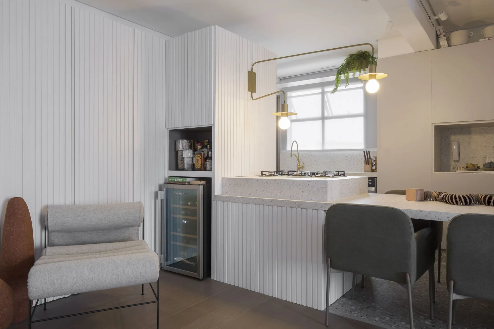 A modern kitchen featuring a white slatted island with a terrazzo countertop, a built-in wine fridge, and a brass swing-arm wall light.