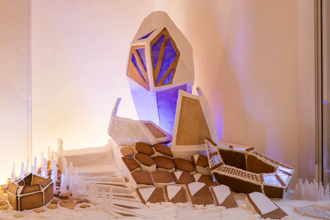 A miniature geometric display of gingerbread-like structures featuring a central white crystal tower lit with a blue interior glow on a white base.