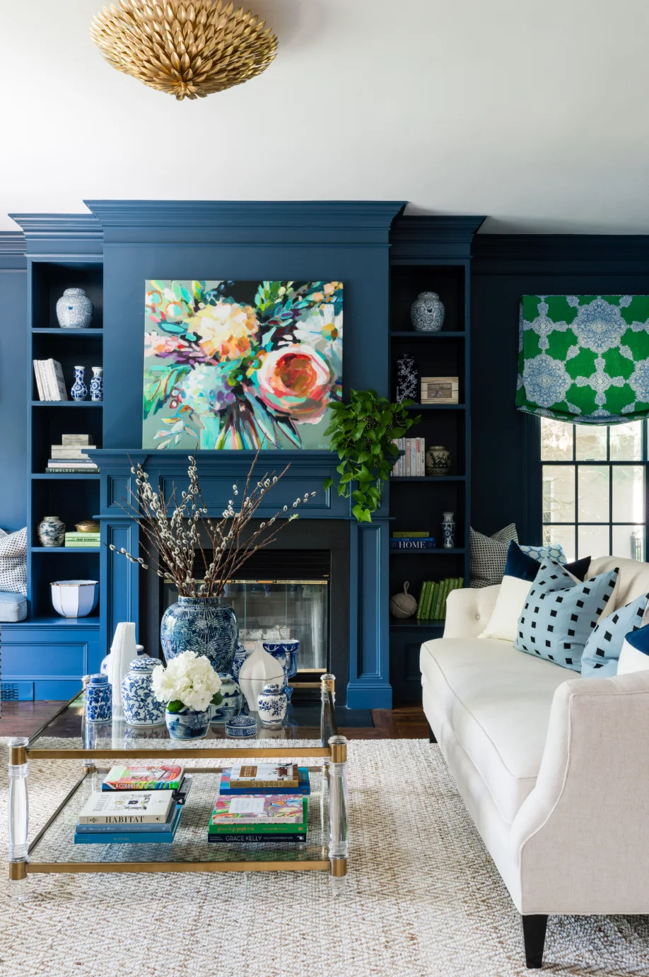 A living room features a navy blue built-in shelving unit surrounding a fireplace, a cream sofa with patterned pillows, and a glass coffee table.