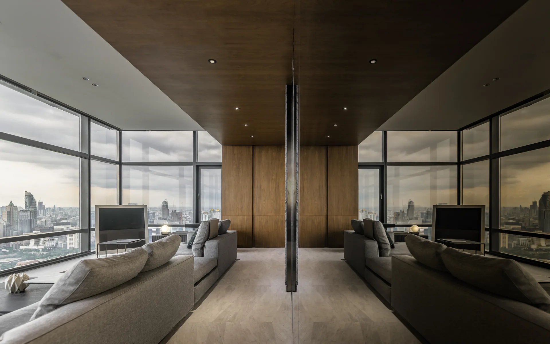 A modern, symmetrical living room features grey sofas, floor-to-ceiling windows with city views, and a central wood-paneled wall and ceiling.