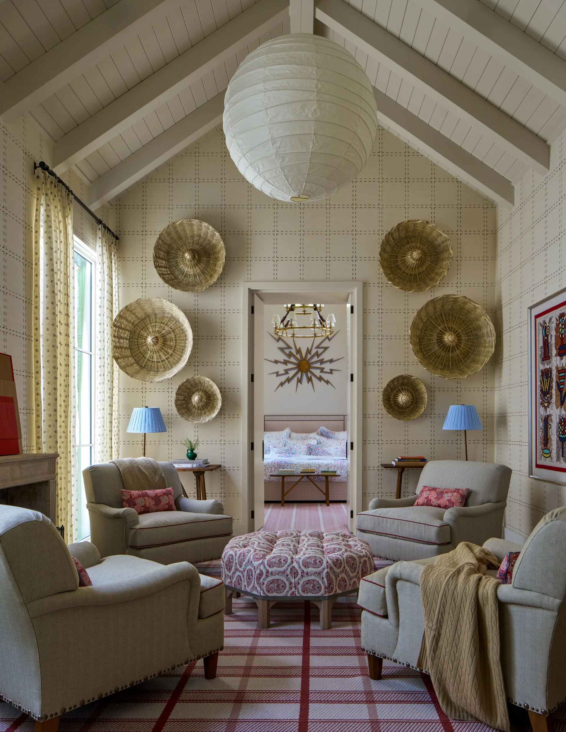 Four cream armchairs and a patterned red ottoman sit under a vaulted ceiling in a room decorated with woven wall baskets.