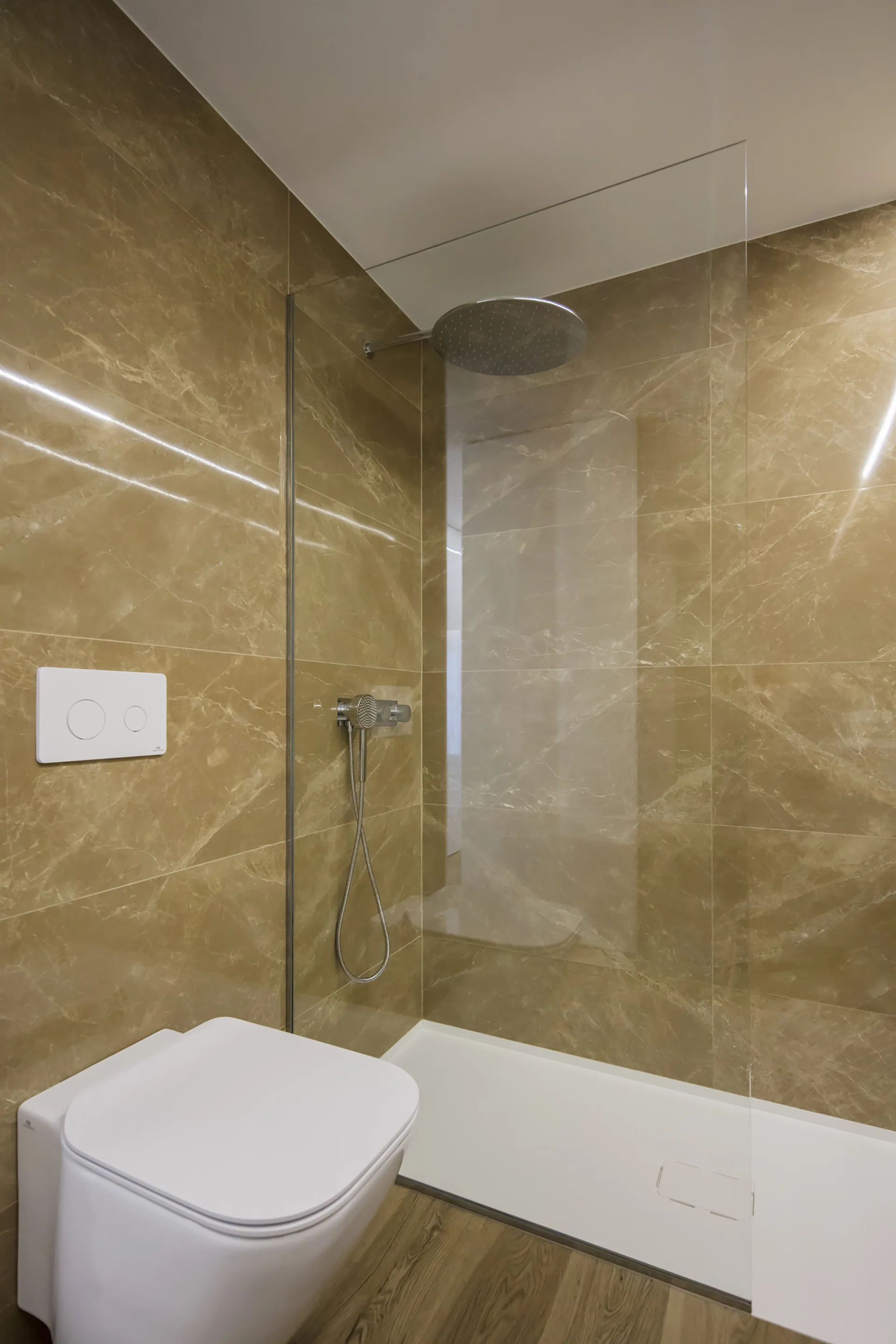 A modern bathroom featuring glossy brown marble-look wall tiles, a frameless glass shower enclosure, and a wall-mounted toilet.
