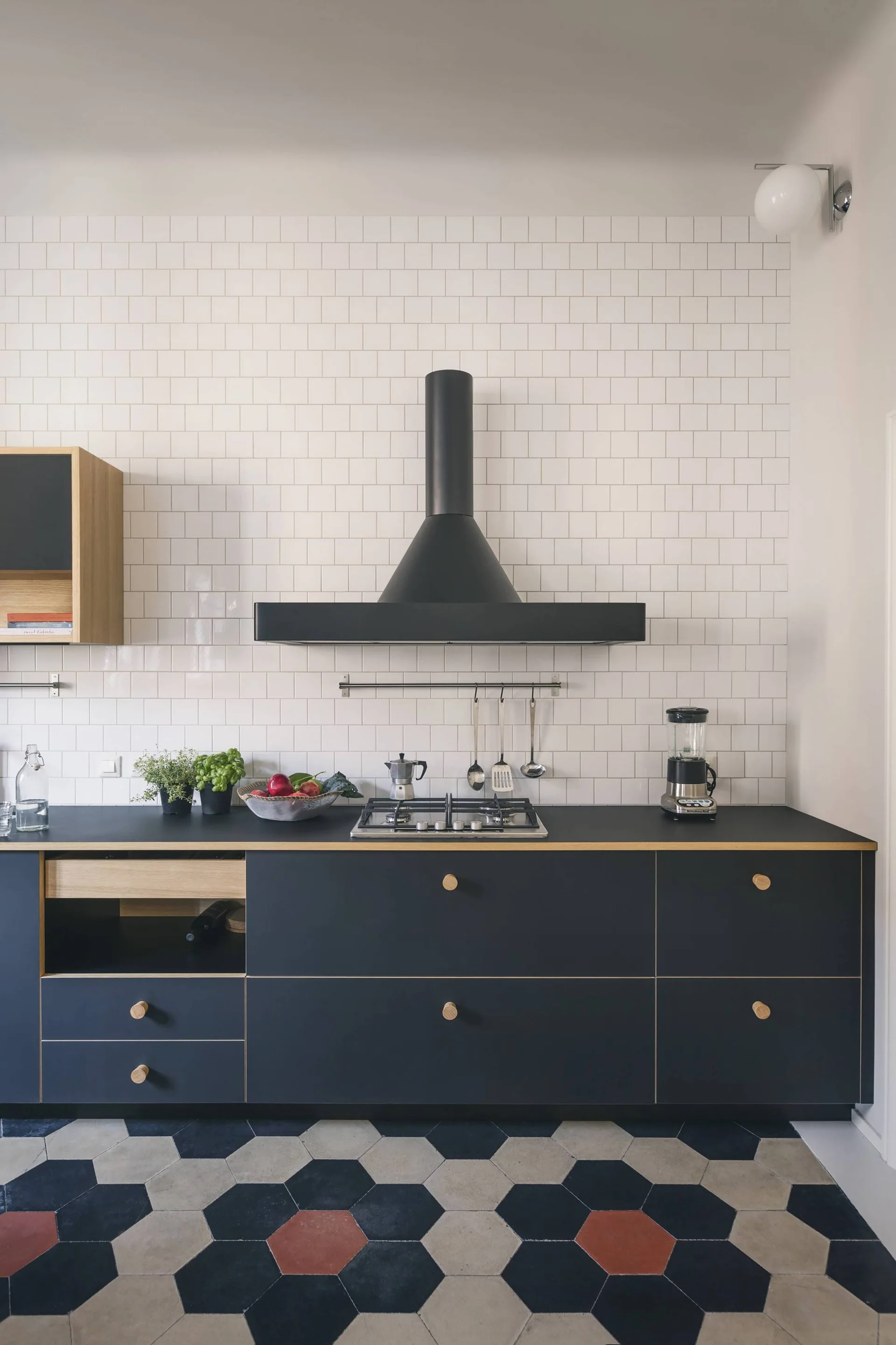 A modern kitchen features navy blue base cabinets with round wood knobs, a white grid tile backsplash, and hexagonal floor tiling.