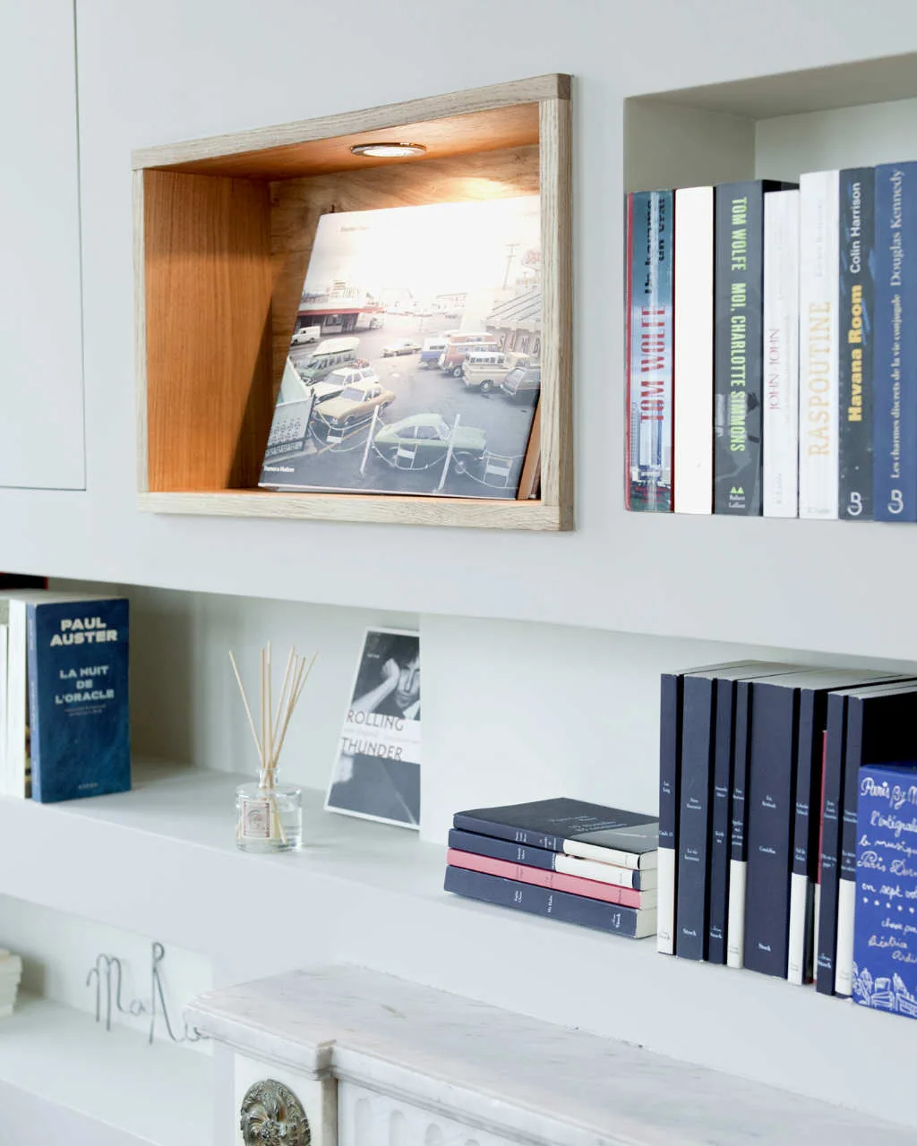 A close-up of white built-in bookshelves featuring an illuminated natural wood niche displaying a book, with other novels stacked neatly alongside.