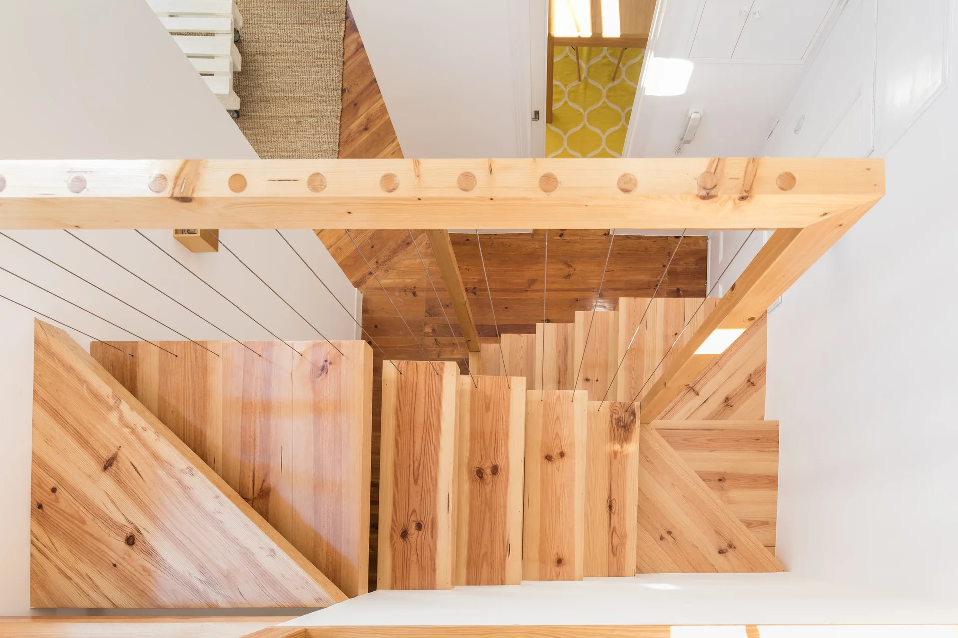 Looking down a light wood staircase with natural finish treads and a wooden handrail featuring thin metal cable balusters.