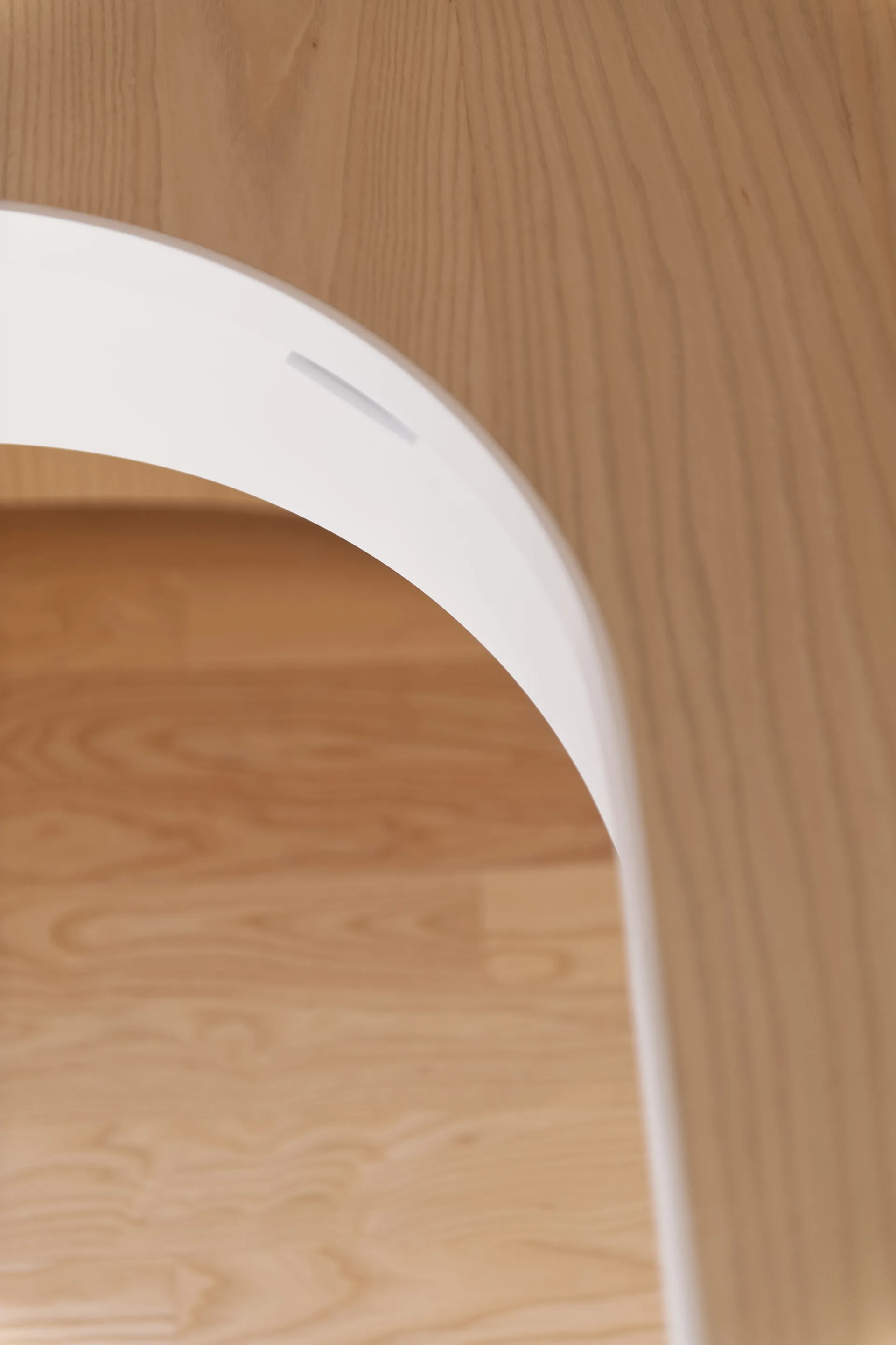 A close-up of a smooth white curved archway set against a light-toned wood paneled wall and floor.
