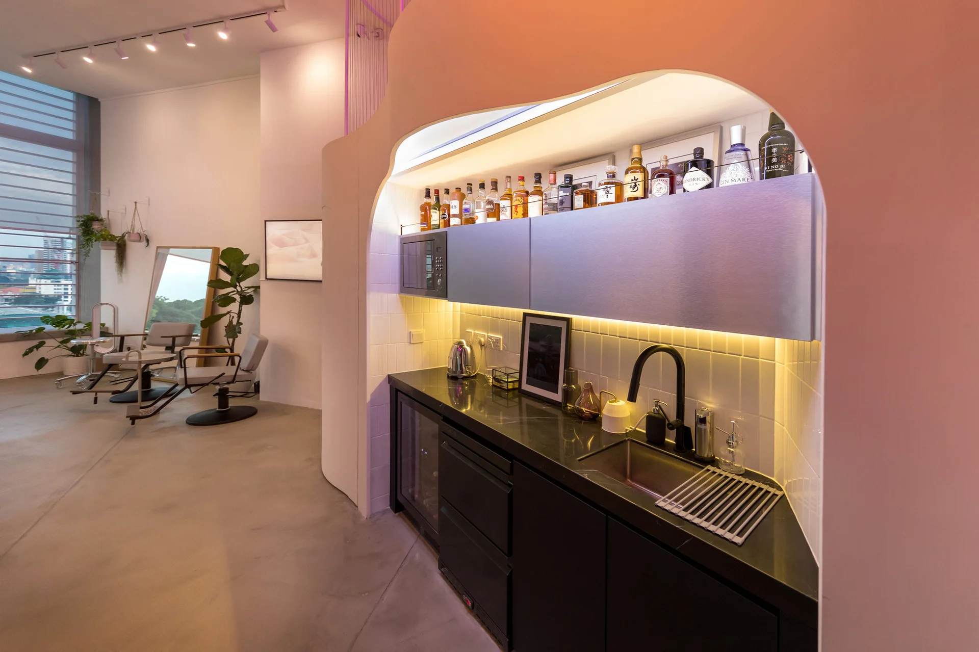 A modern wet bar with black countertops, metallic upper cabinets, and a white tile backsplash is recessed inside a curved partition wall.