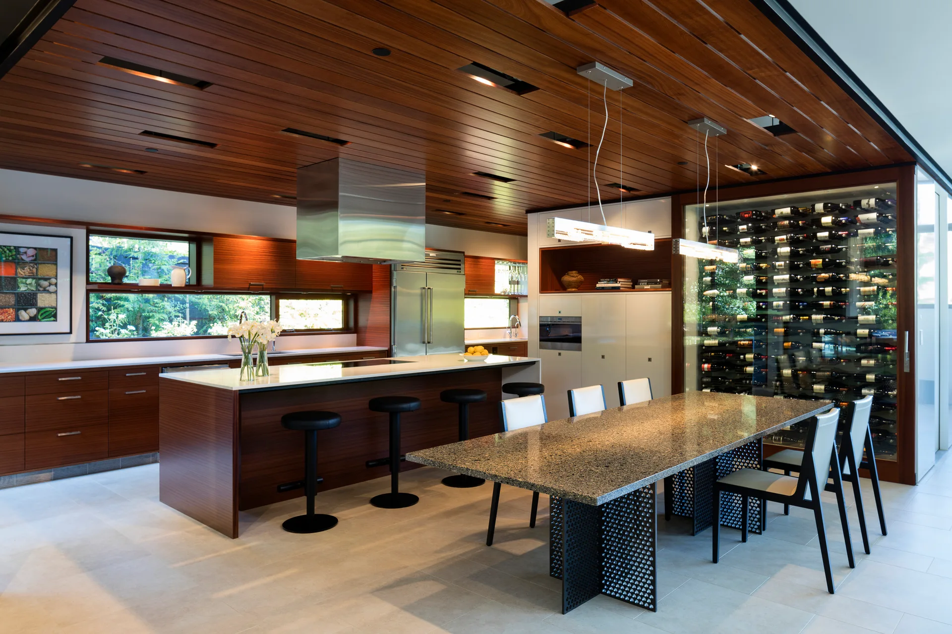 A contemporary kitchen and dining space featuring a warm wood plank ceiling, a central island, and a glass-enclosed wine wall.