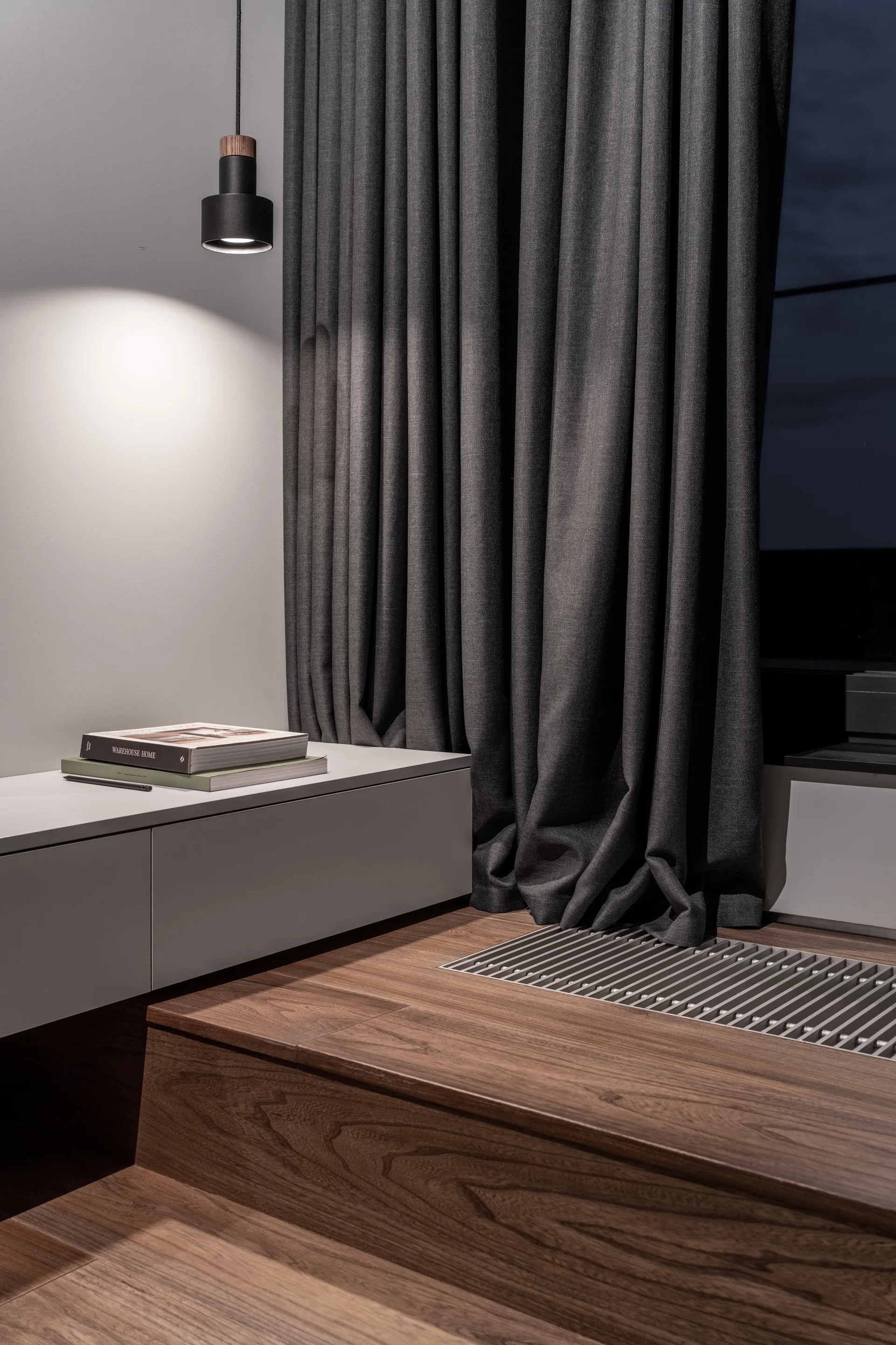 A wall-mounted grey cabinet next to long charcoal grey curtains pooling on a raised wooden floor with an integrated metal vent.