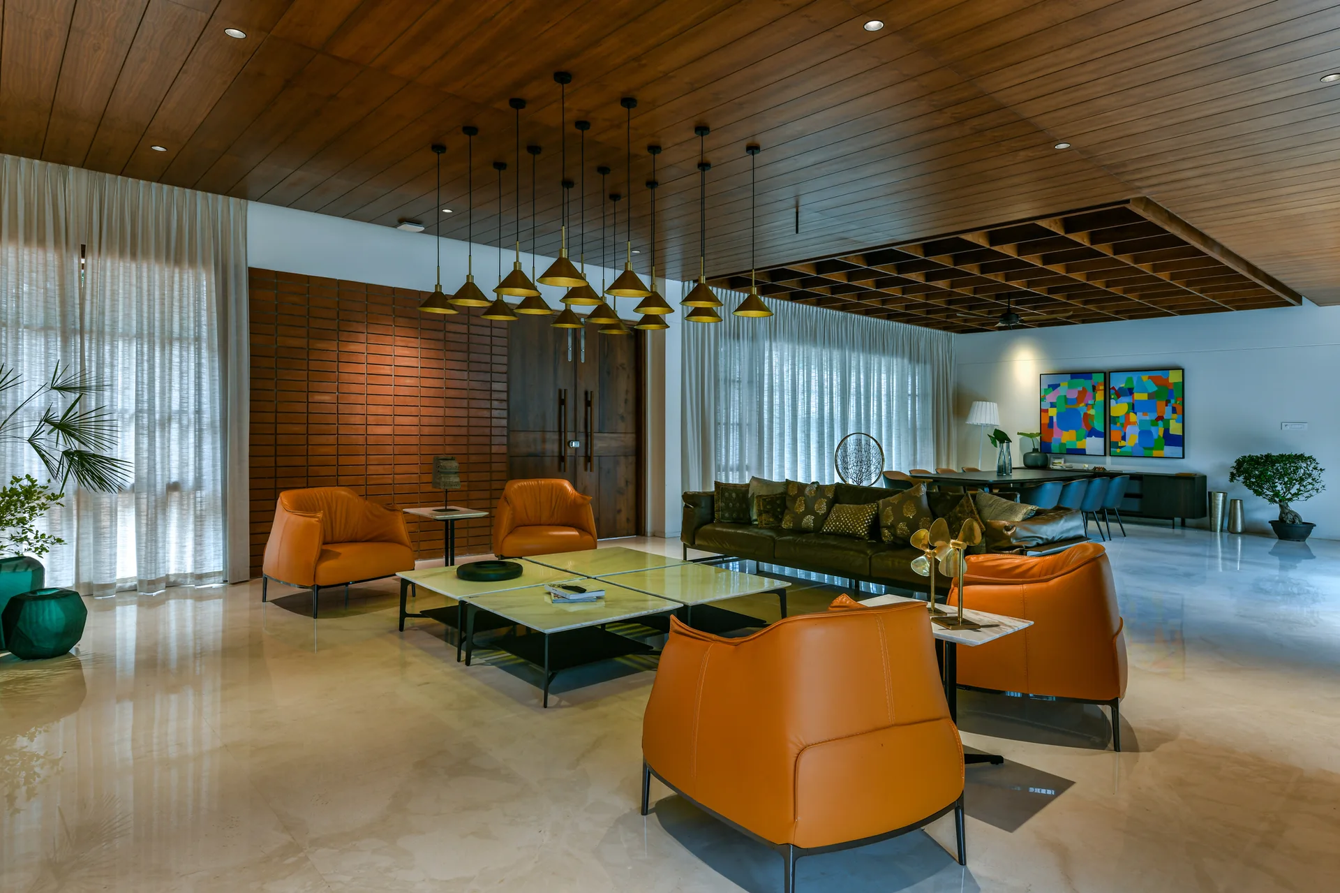 A spacious living room features orange leather armchairs, a wood paneled ceiling, a green sofa, and a large cluster of brass pendant lights.