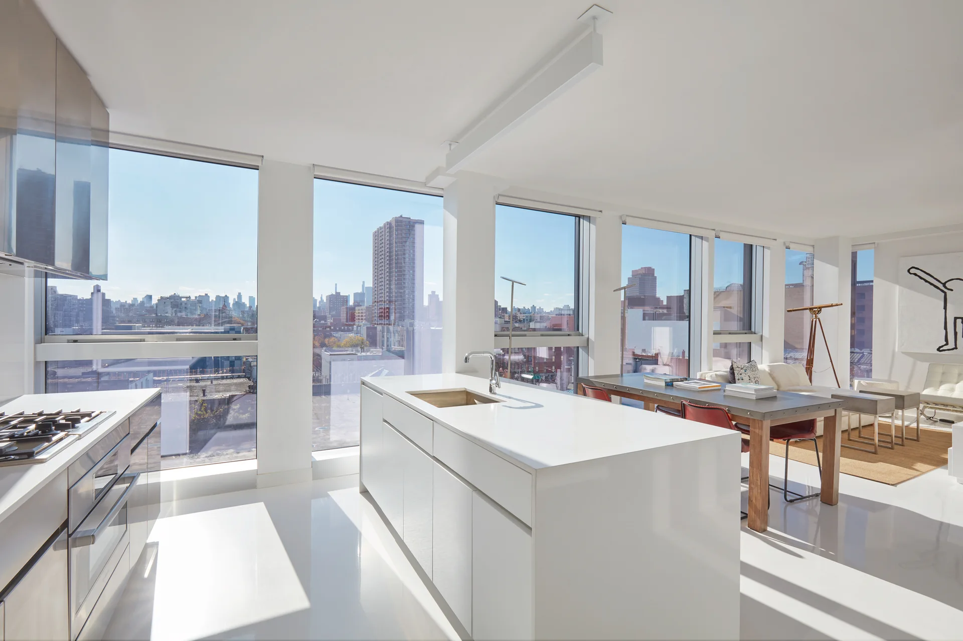 An open-concept kitchen and dining area features a white island, glossy white floors, a wood dining table, and large windows with a city view.