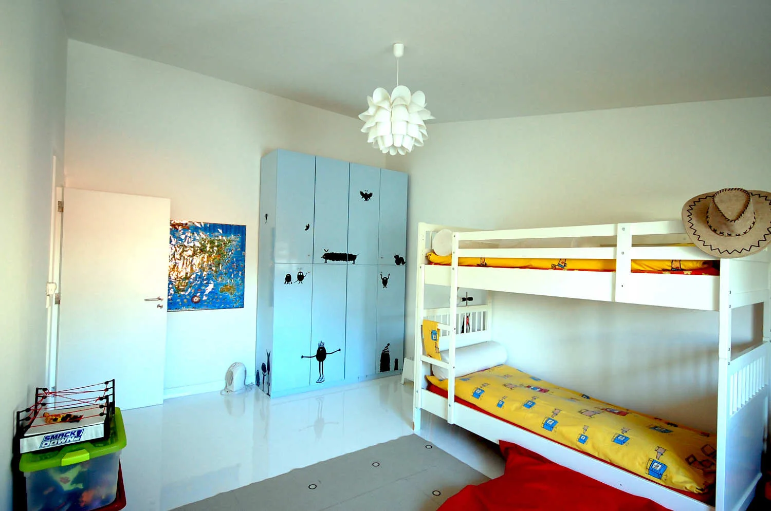 A children's bedroom features a white wooden bunk bed with yellow bedding next to a light blue wardrobe decorated with small black character illustrations.