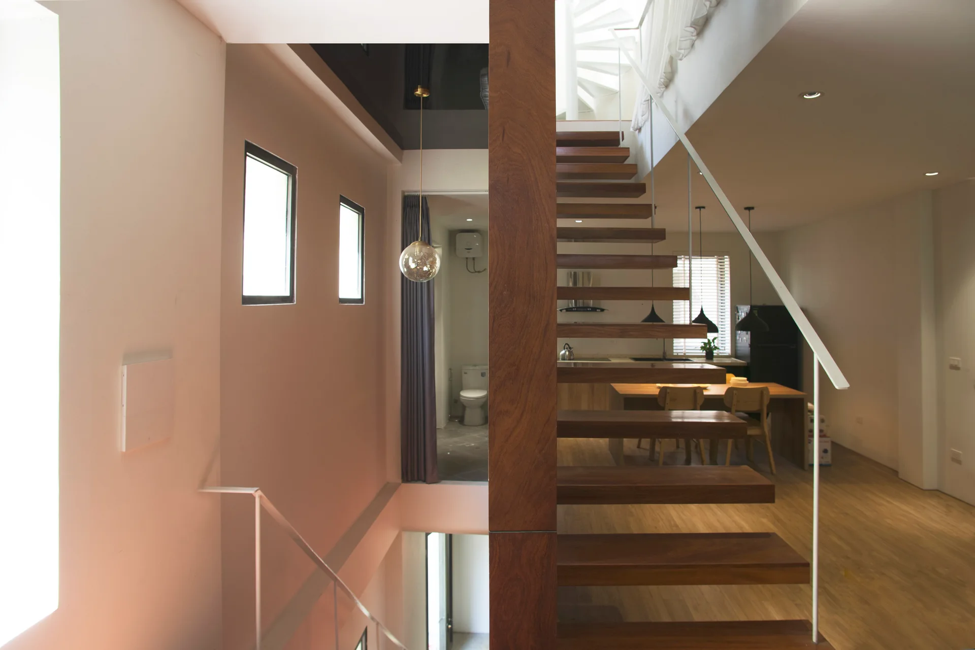 A modern home interior showcasing a floating wooden staircase with open risers, a central wood pillar, and a slim white handrail.