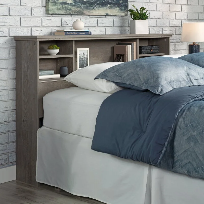 A grey wood storage headboard with built-in shelves sits against a white painted brick wall next to a bed dressed in blue and white bedding.