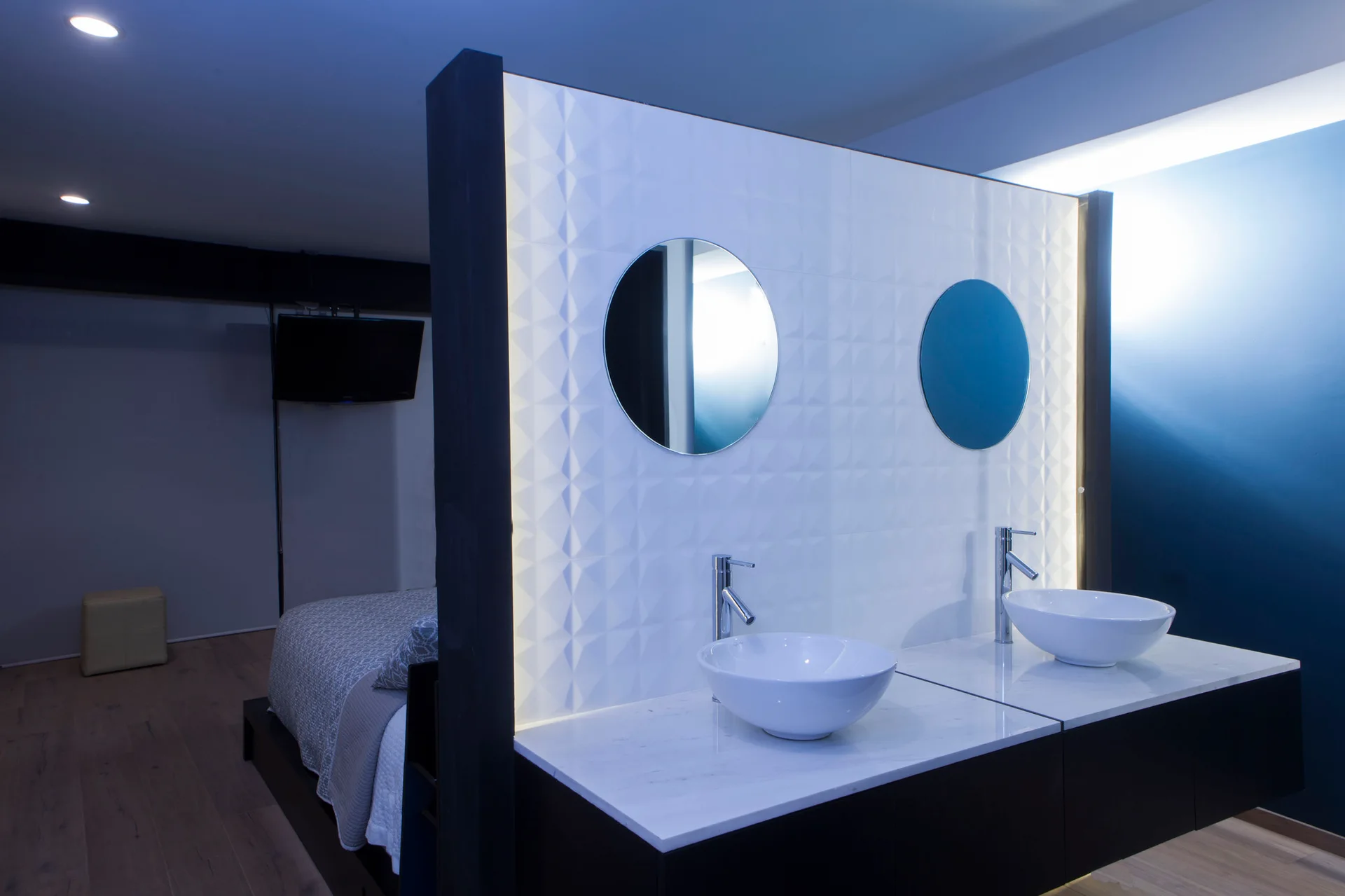 A modern bathroom vanity with two white vessel sinks and round mirrors sits against a geometric tiled partition wall.