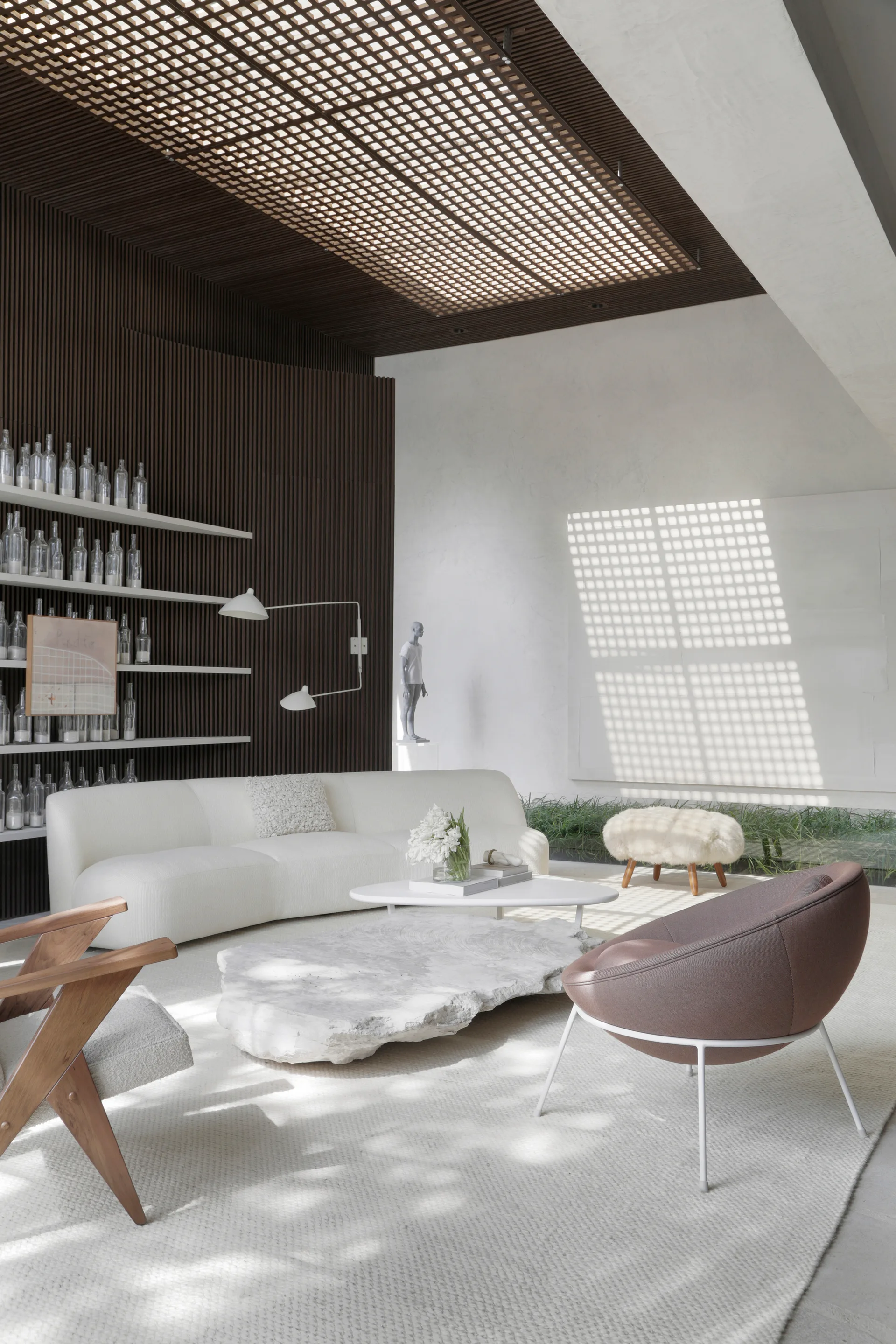 A modern living room features a white curved sofa, an irregular stone coffee table, a dark wood slatted wall, and a grid skylight overhead.