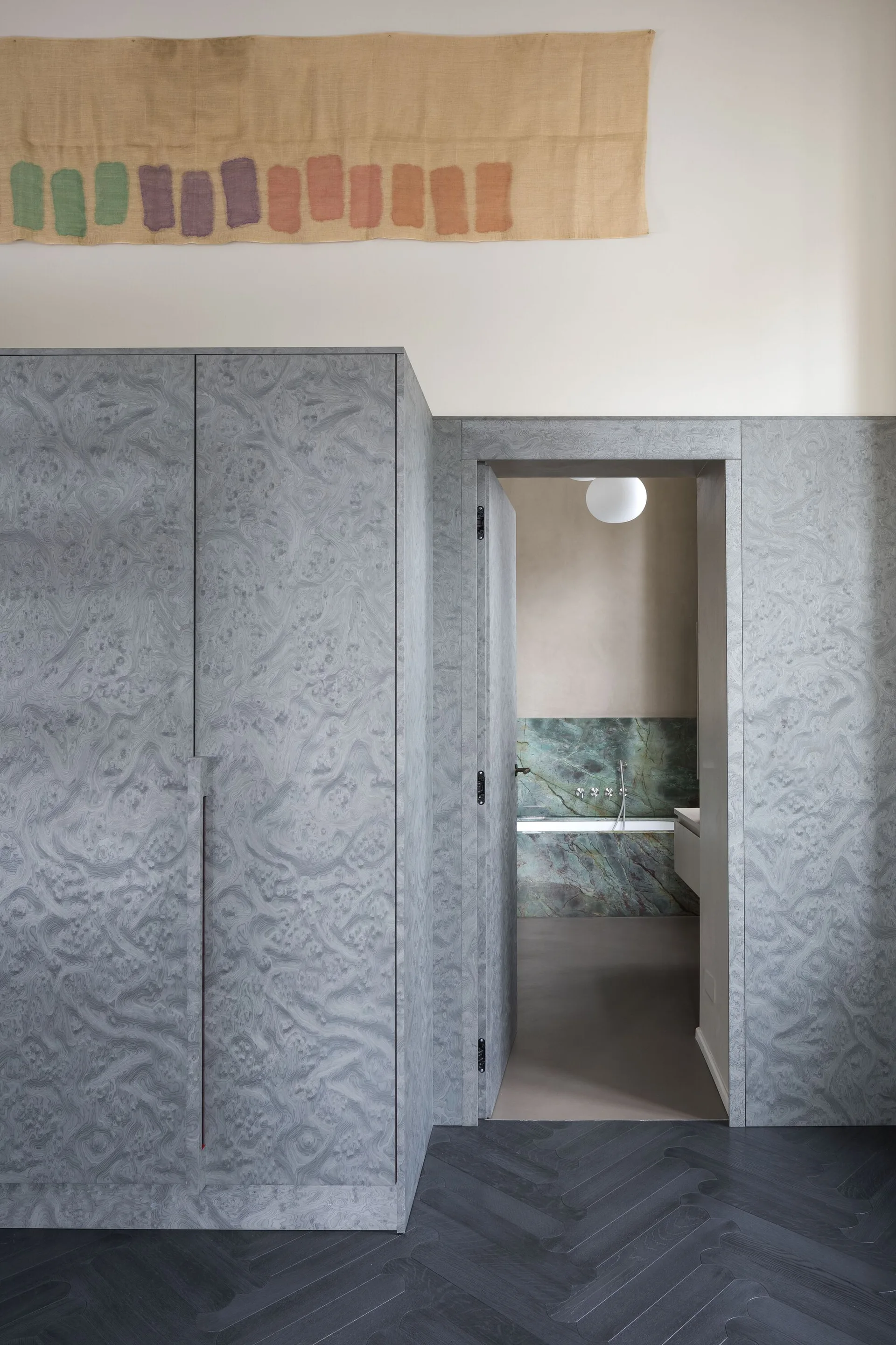Grey swirled pattern built-in cabinets flank an open doorway leading to a bathroom with a green marble tub backsplash.