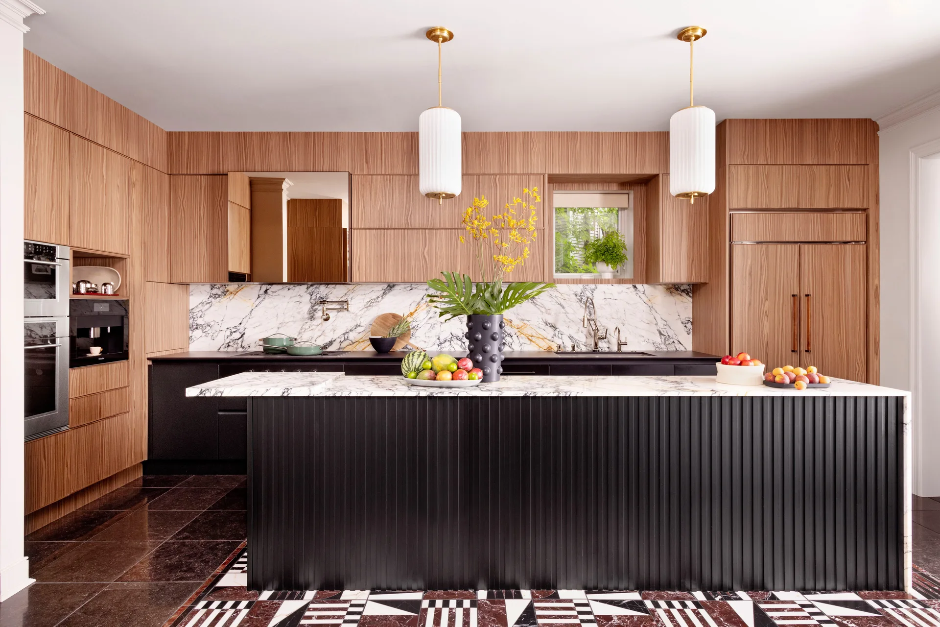 A modern kitchen featuring floor-to-ceiling wood cabinetry, a black ribbed island with a white marble top, and bold geometric floor tiles.