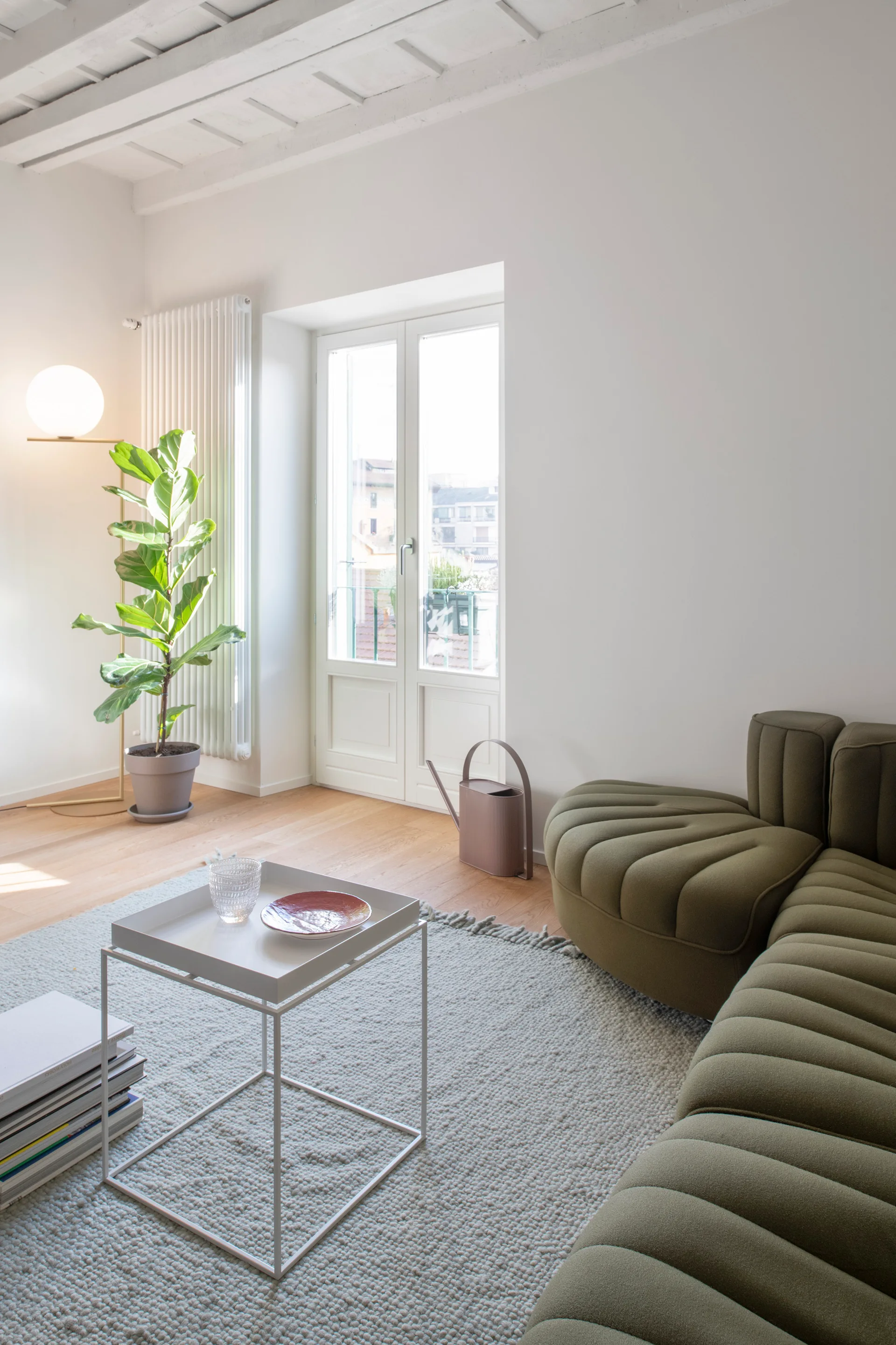An olive green channeled modular sofa sits on a grey textured rug next to a white tray coffee table and a potted fiddle-leaf fig tree.