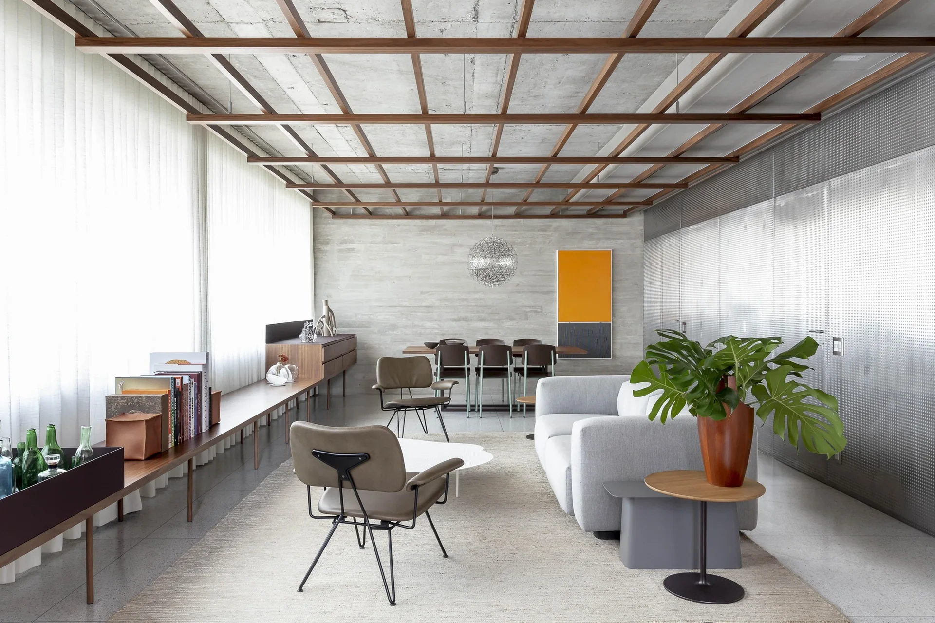 A modern living and dining space featuring a grey sofa, leather armchairs, and a wood grid ceiling over concrete.