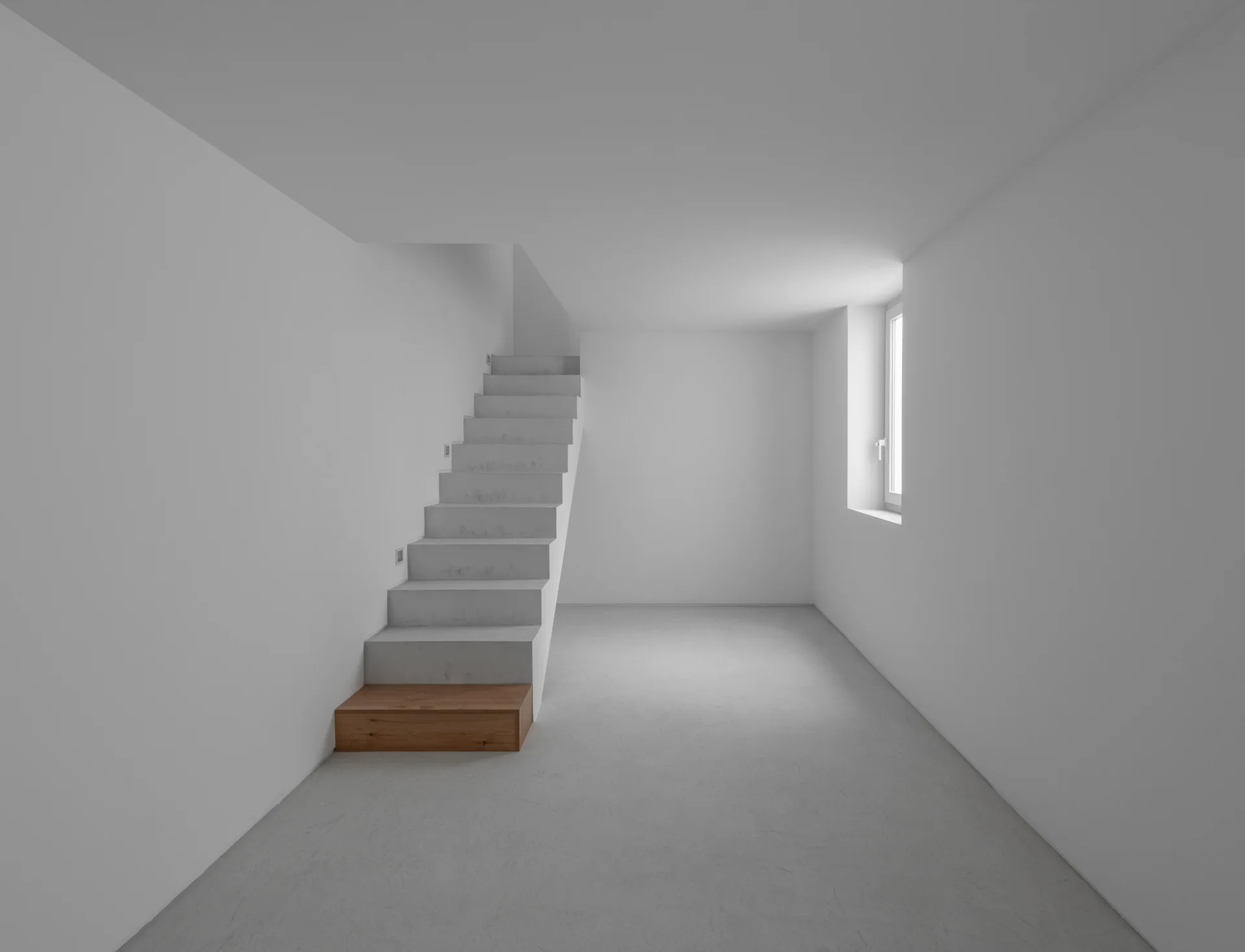 A minimalist white staircase features a single warm wood-toned bottom step in an empty room with grey concrete floors.