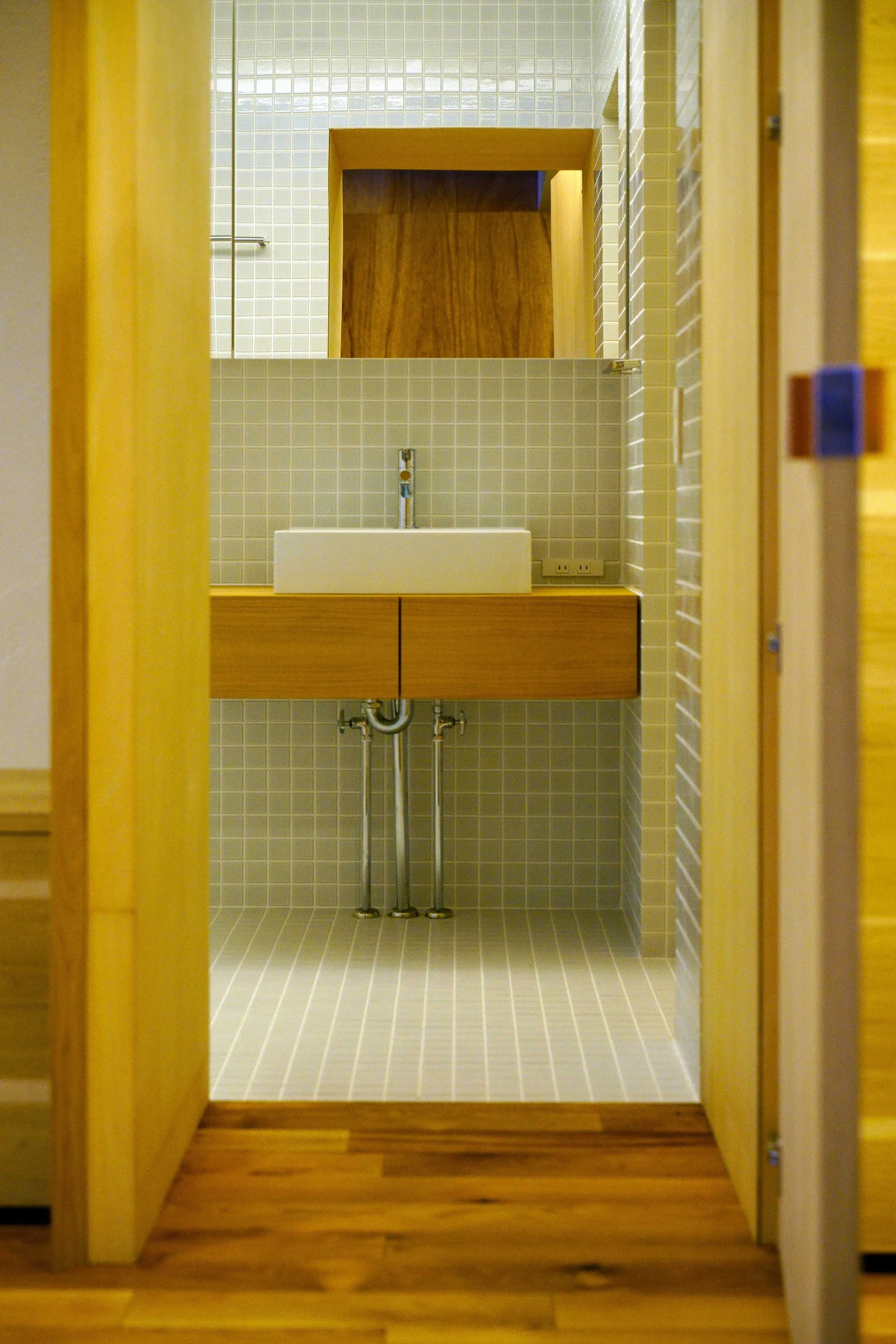 A rectangular white vessel sink sits on a floating wood vanity against a wall covered in light gray square grid tiles.