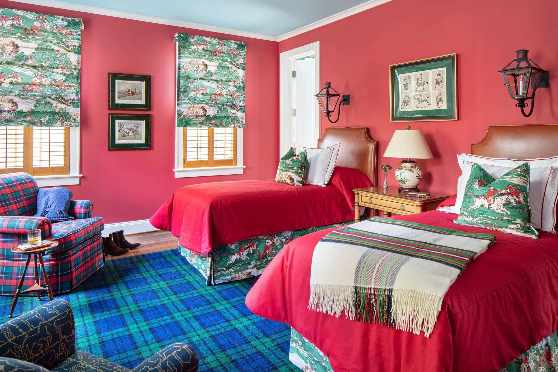 A red bedroom features two twin beds with leather headboards, equestrian print accents, and a large blue and green plaid carpet.