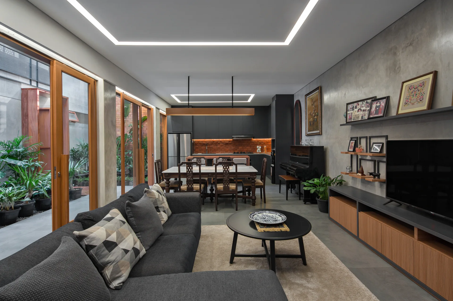 An open-concept living space with concrete walls, a dark grey sectional sofa, and wood-framed sliding glass doors opening to an outdoor courtyard.